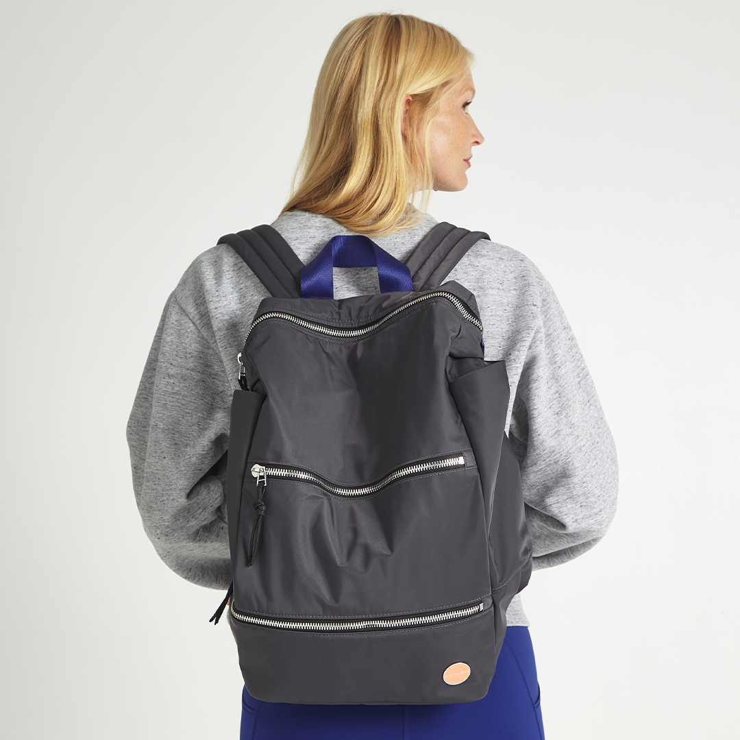 Person wearing a charcoal backpack on a plain background