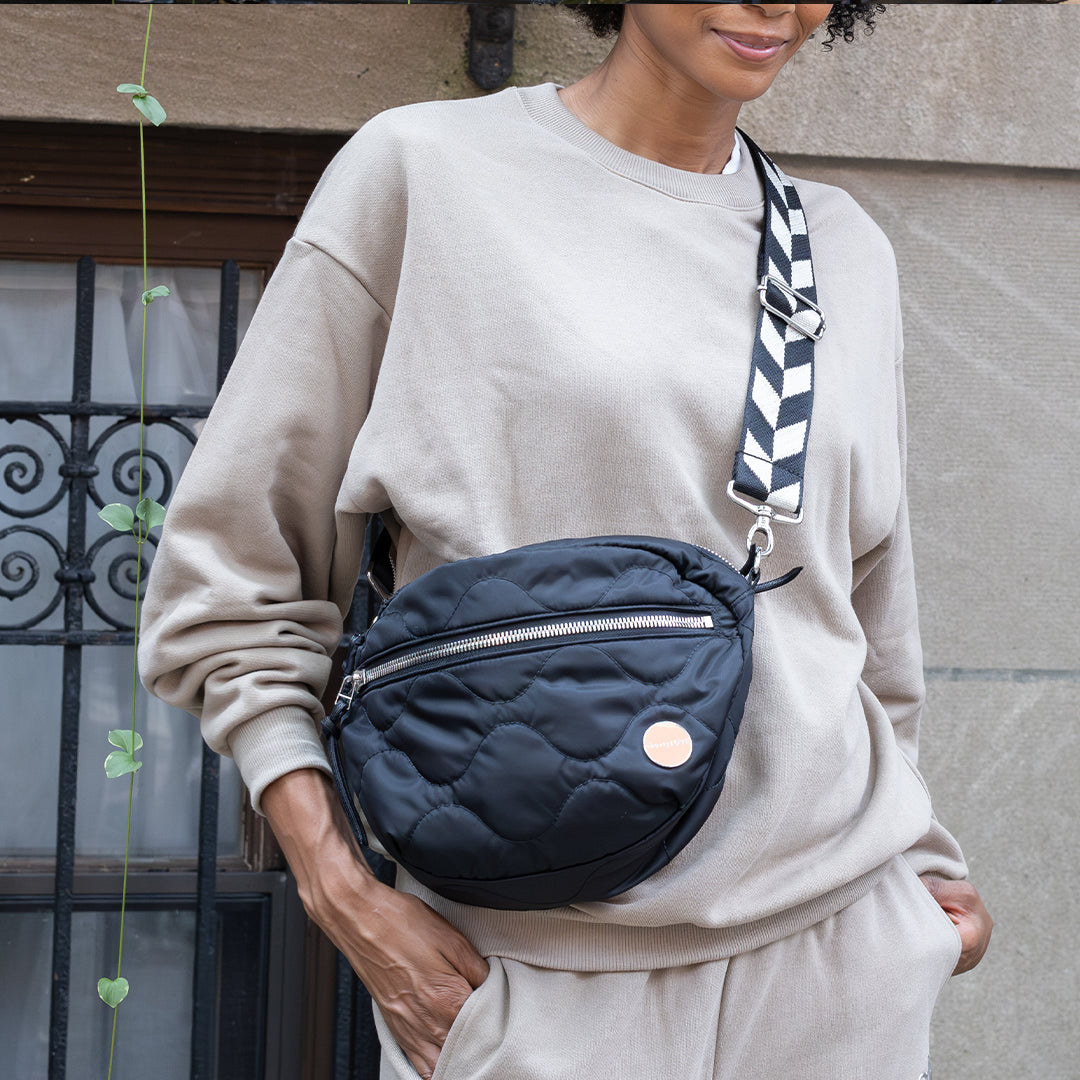 Person wearing a beige sweatshirt and holding a black cruiser quilted bag with a striped strap.