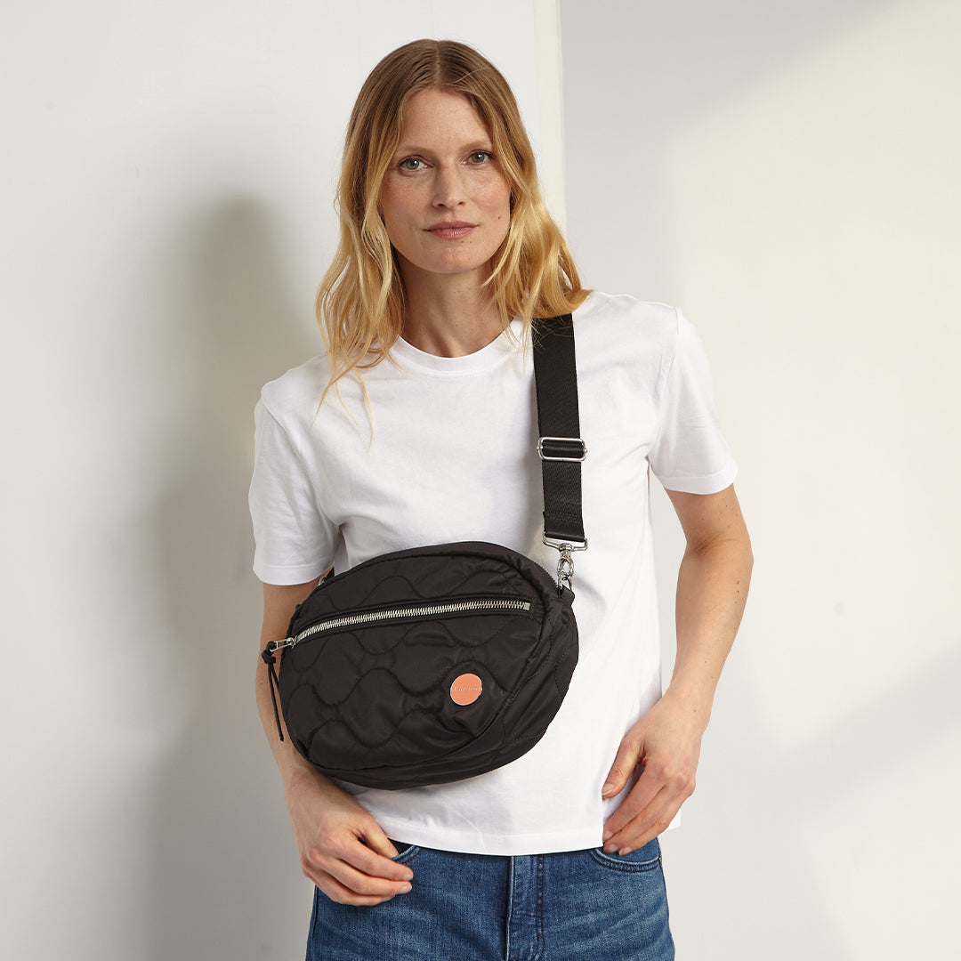 Woman holding a black quilted cruiser bag against a plain background