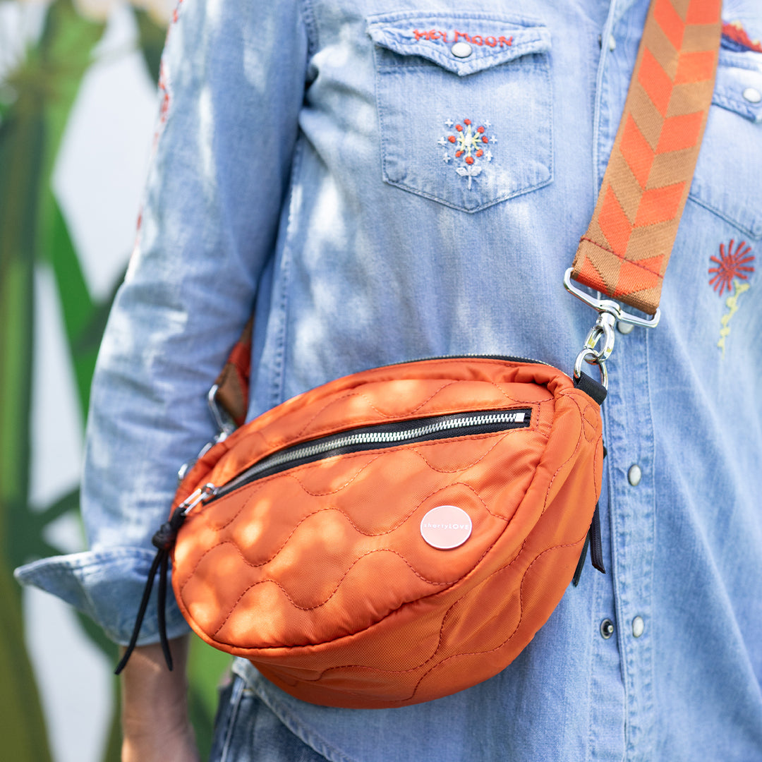 Person wearing an orange quilted cruiser crossbody bag with a denim jacket.