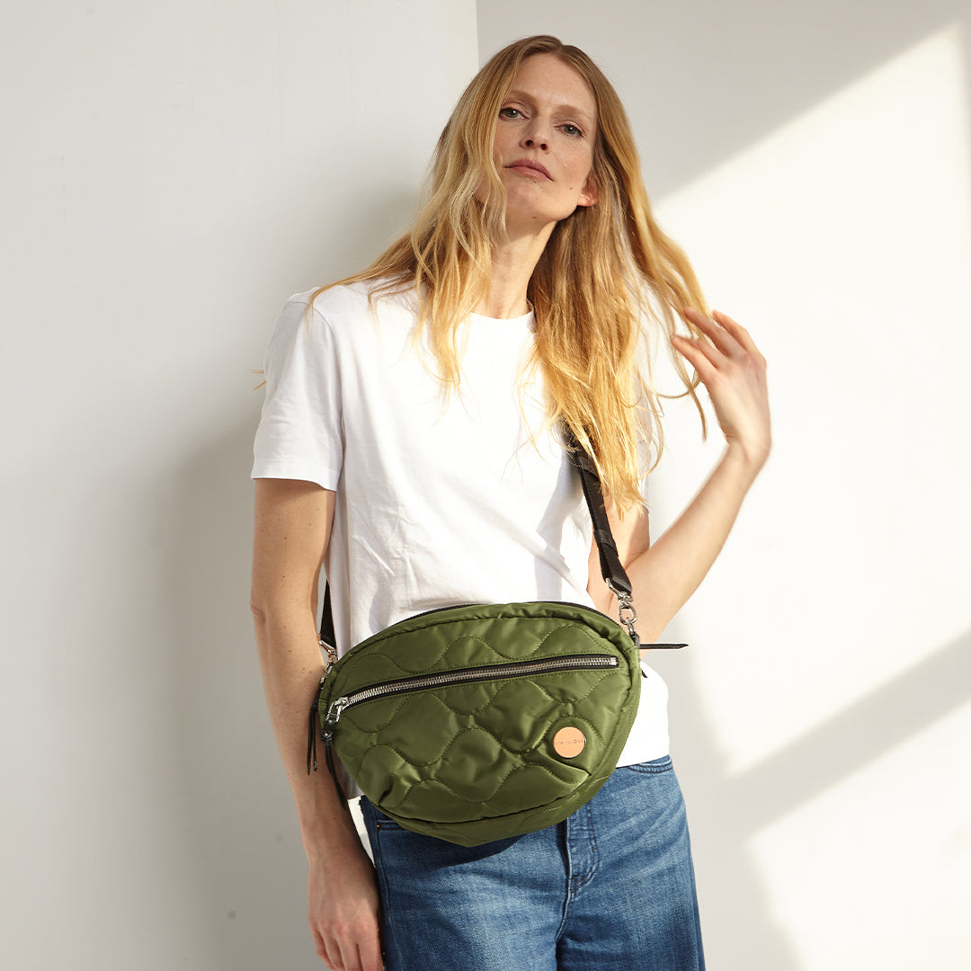 Woman wearing a sage quilted cruiser crossbody bag against a white wall