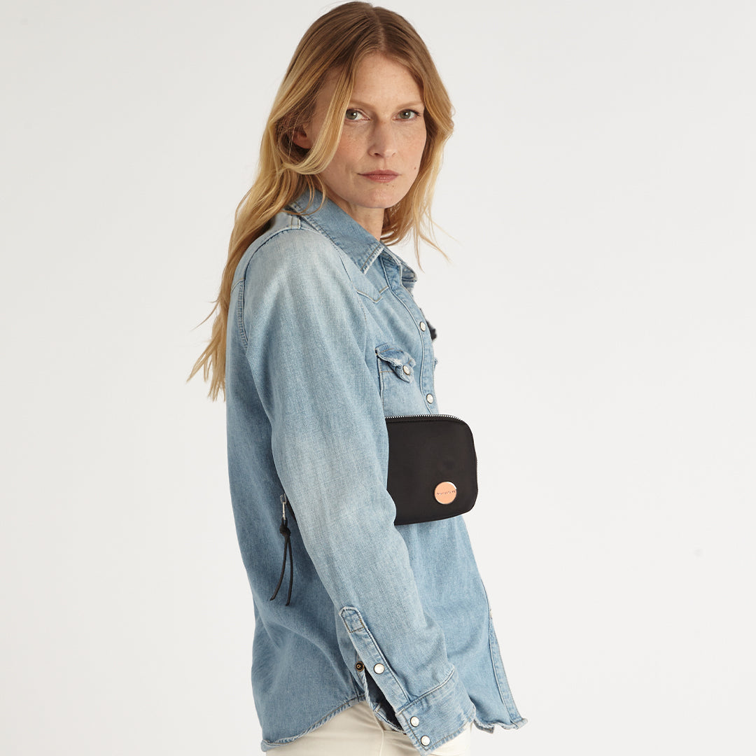 Woman wearing a denim shirt with a black jetty wallet/clutch on a white background