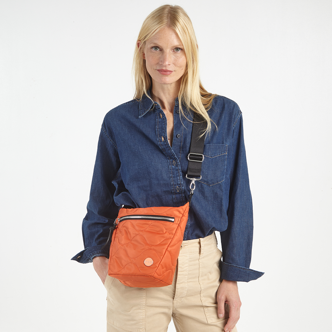 Woman wearing an orange marcel quilted crossbody bag on a white background