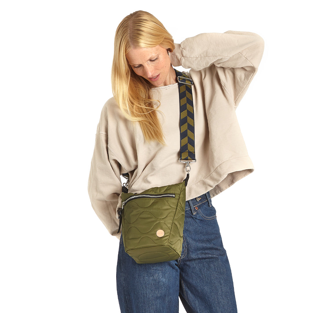 Woman wearing a sage green marcel quilted crossbody bag with a colorful crossbody strap on a white background