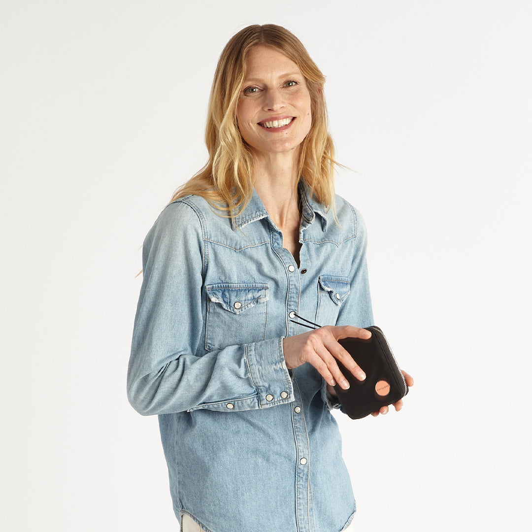 Woman wearing a light blue denim shirt holding a black merchant wallet on a white background