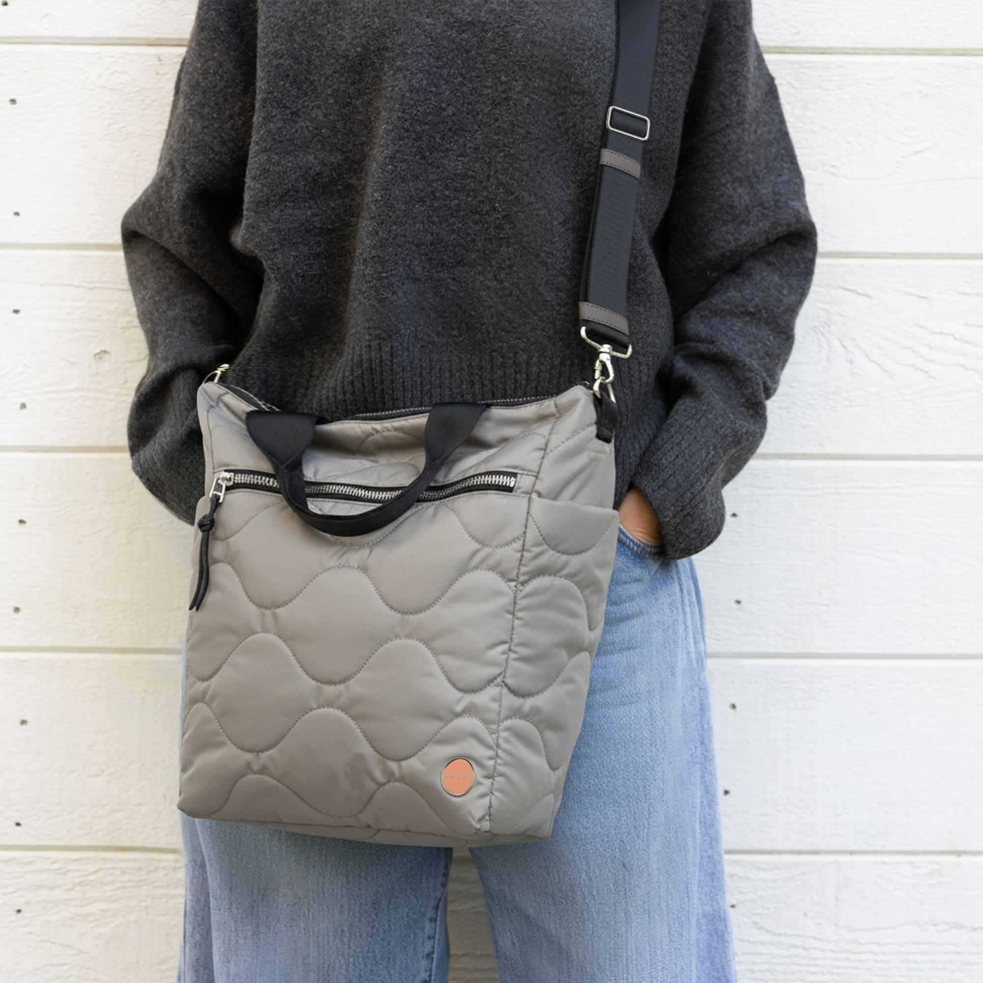 Person wearing a gray quilted ranger tote over one shoulder against a white wooden background