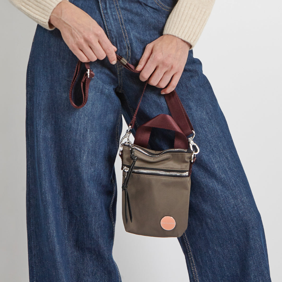 Person holding a small mocha shorthand handbag with a plain background