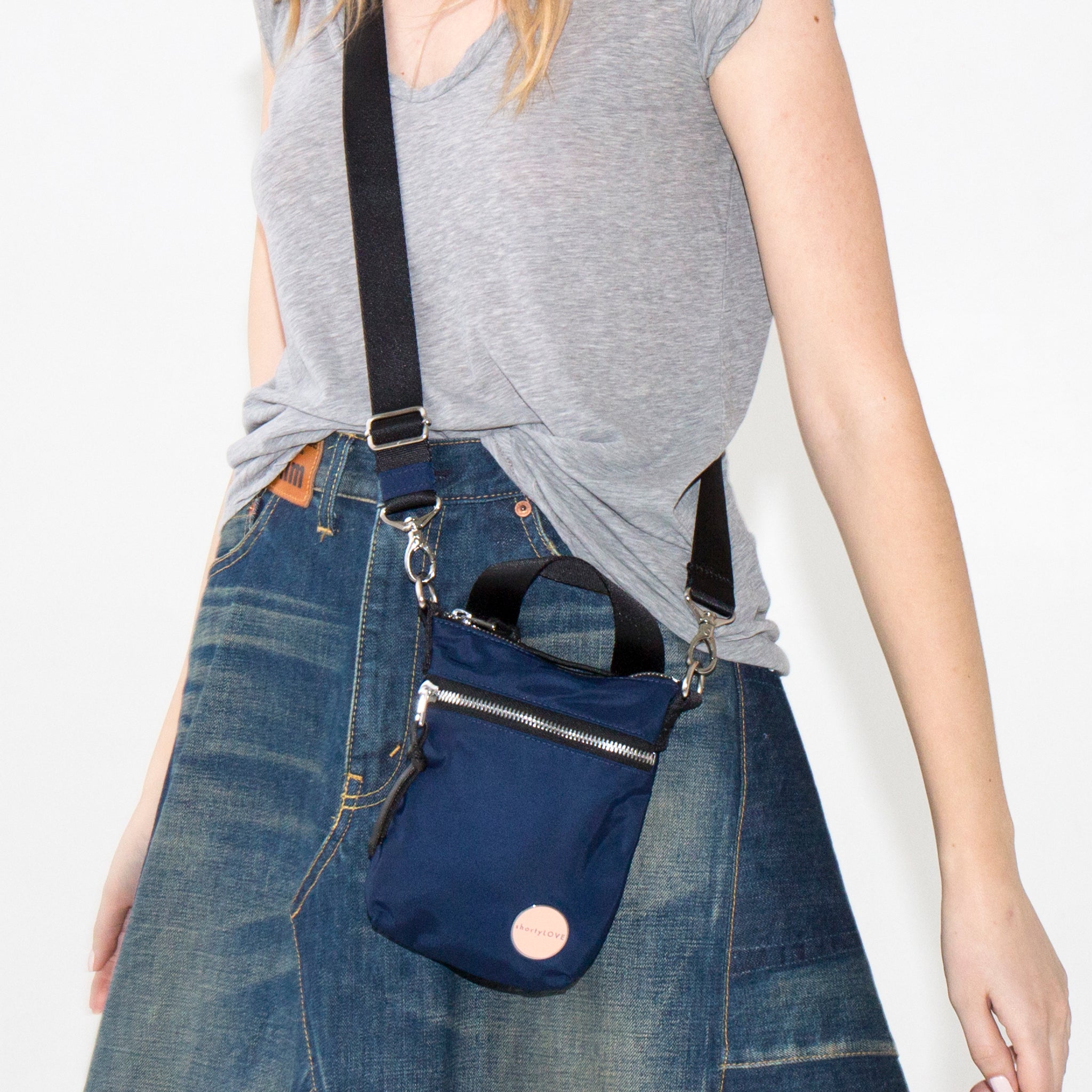 Person wearing a navy blue shorthand crossbody bag with a plain background