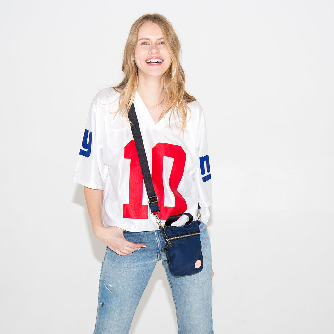 Woman wearing a sports jersey with number 10, holding a navy shorthand crossbody bag on a white background
