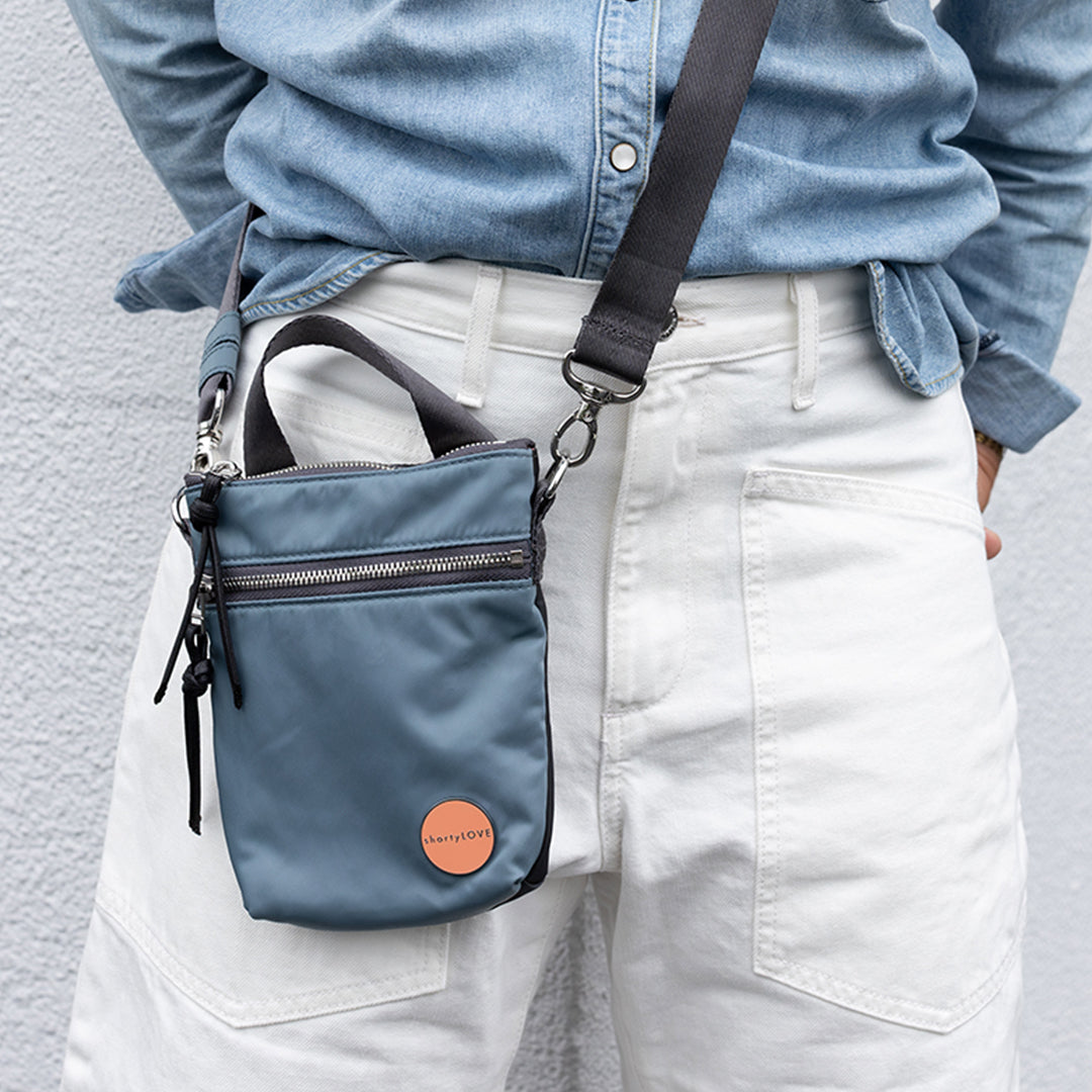 Person wearing a steel blue/ charcoal  shorthand crossbody bag with a visible brand logo against a neutral background