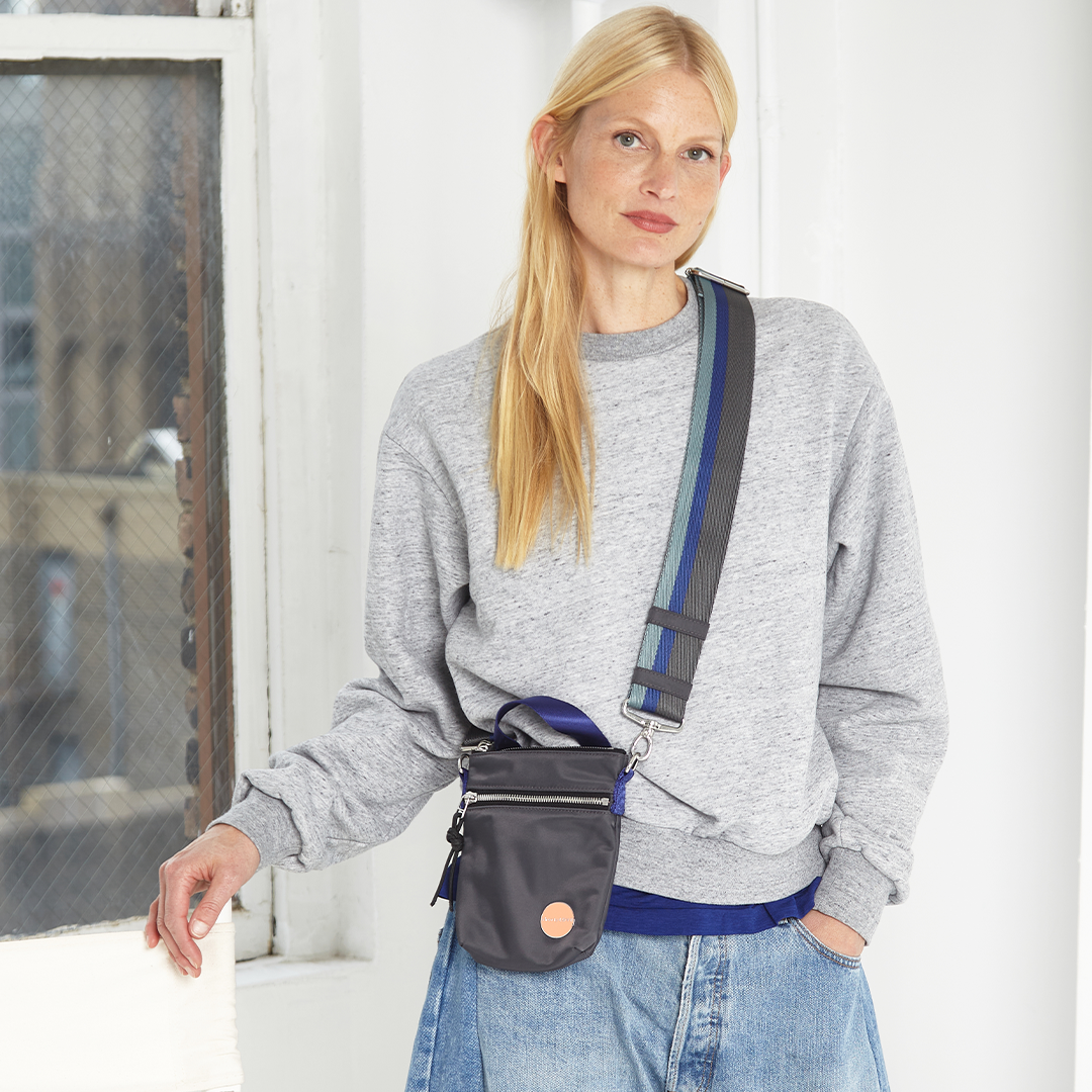 Woman wearing a gray sweatshirt with a charcoal shorthand crossbody bag in an urban setting