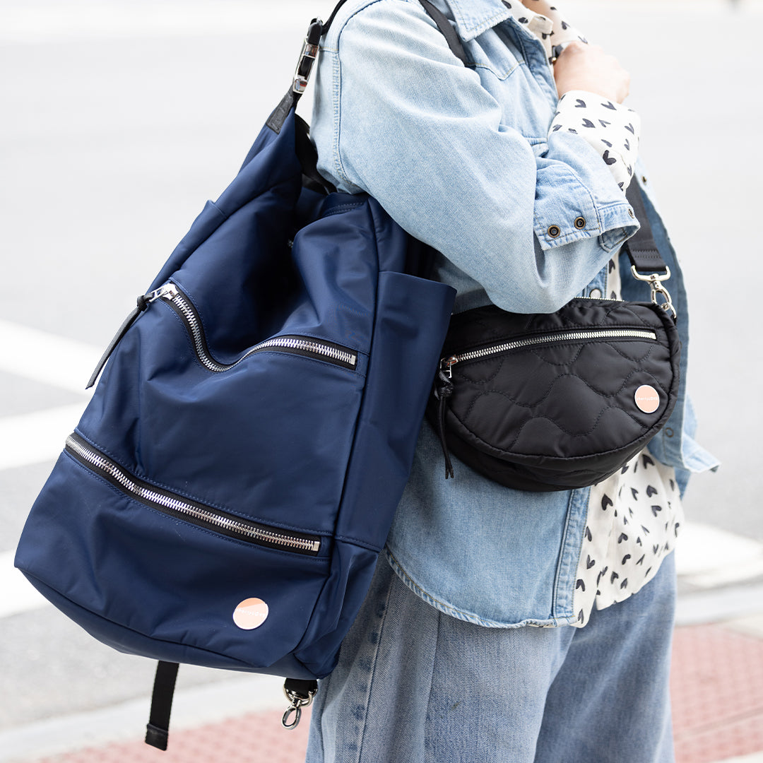 Person carrying a navy blue boxer backpack and a black quilted handbag with a light background