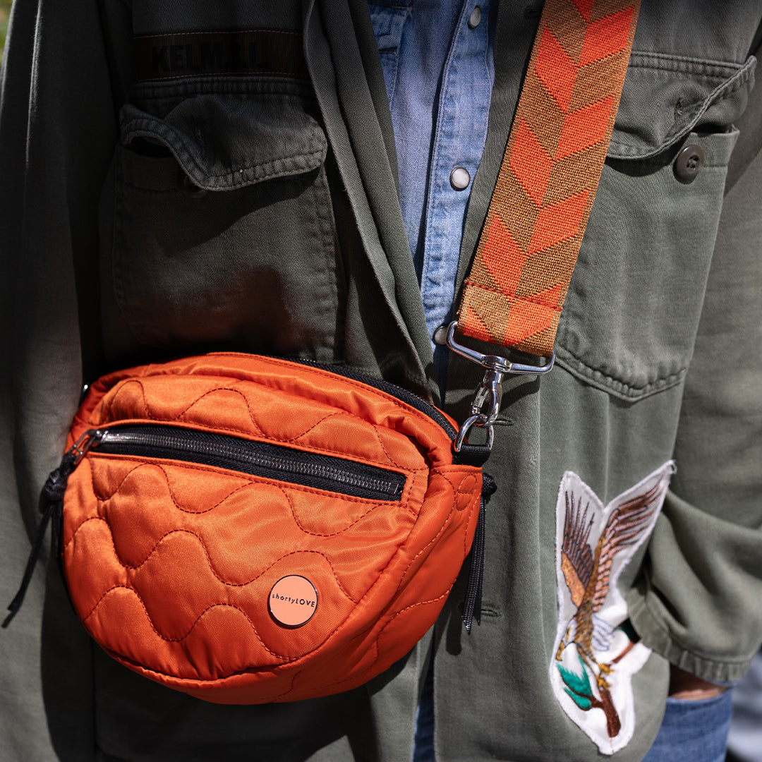 Orange quilted crossbody bag worn by a person with a patterned strap.