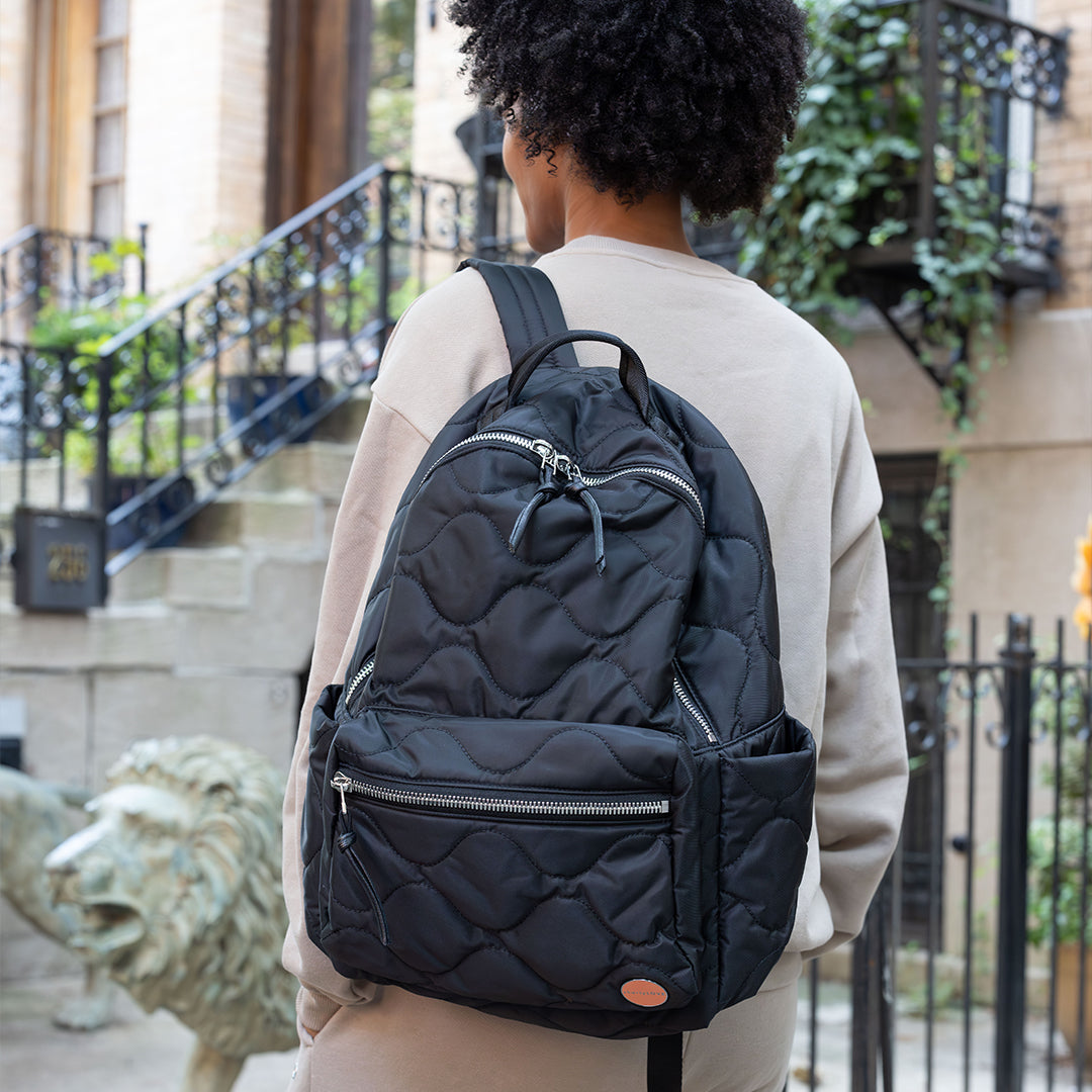 woman wearing a black tate quilted backpack on a city street