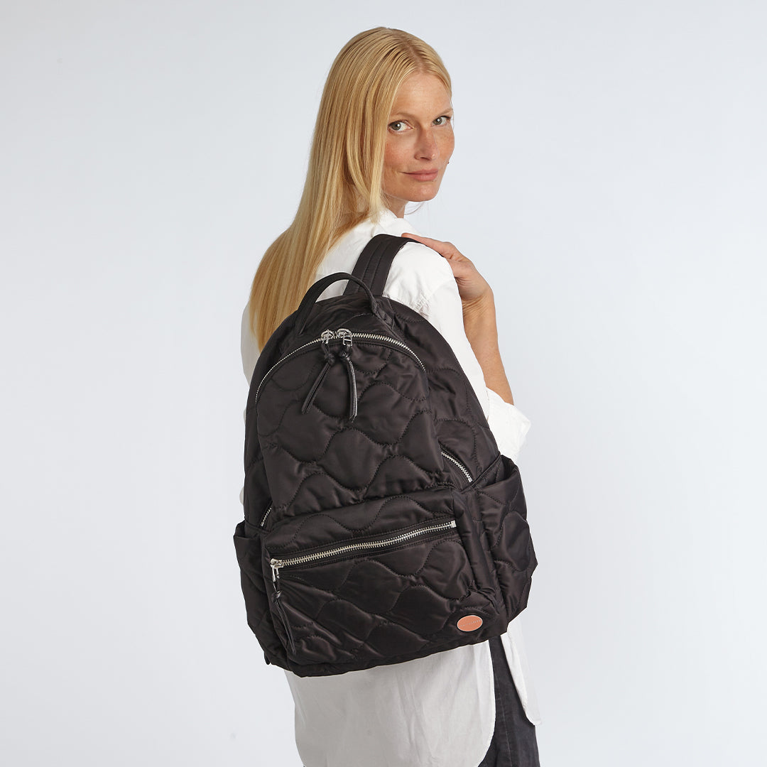 Person wearing a black quilted tate backpack on a white background