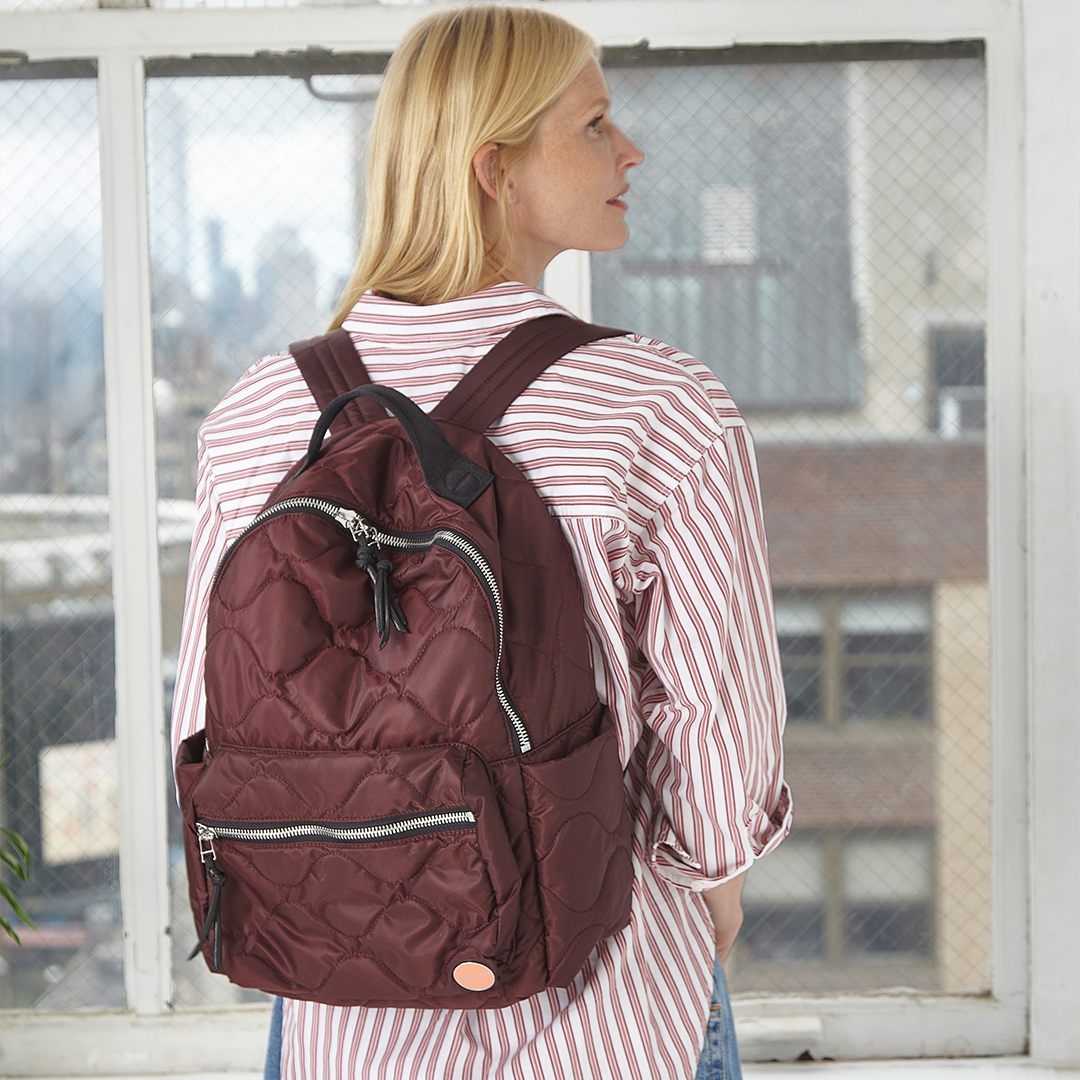 Woman wearing a maroon/bordeaux backpack in an urban setting