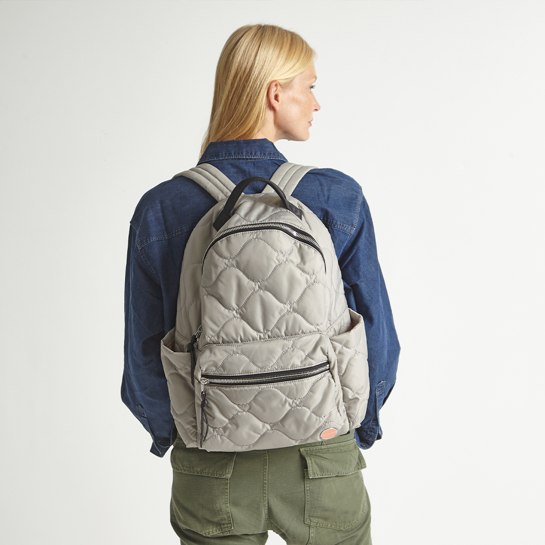 Person wearing a gray quilted tate backpack on a plain background