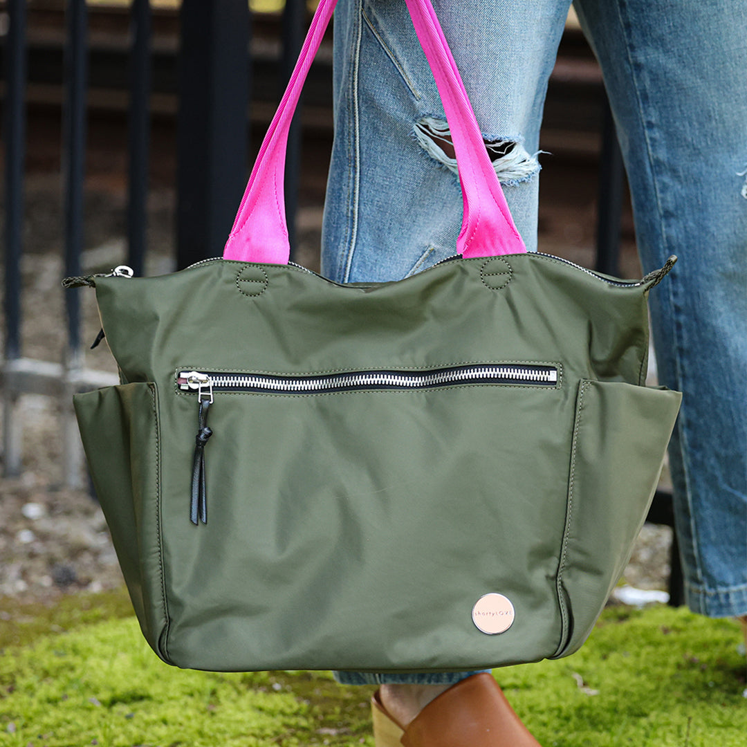 army green tillie tote bag with pink straps held by a person wearing blue jeans.