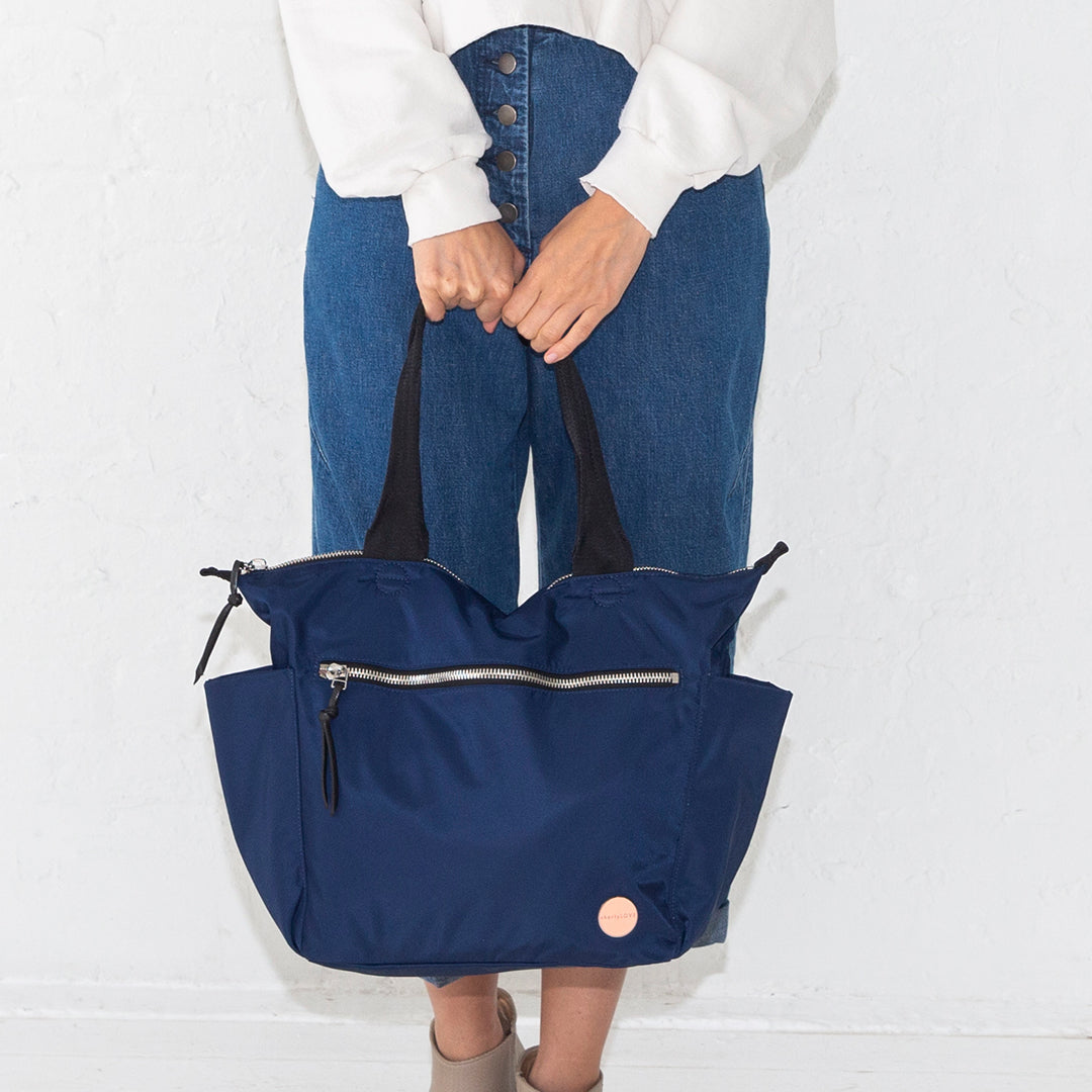 Person holding a navy blue tillie tote bag against a white background