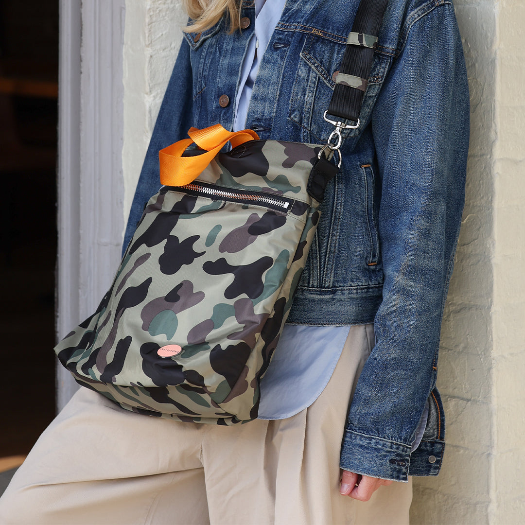 Person wearing a camouflage wonder crossbody bag over one shoulder with a denim jacket.