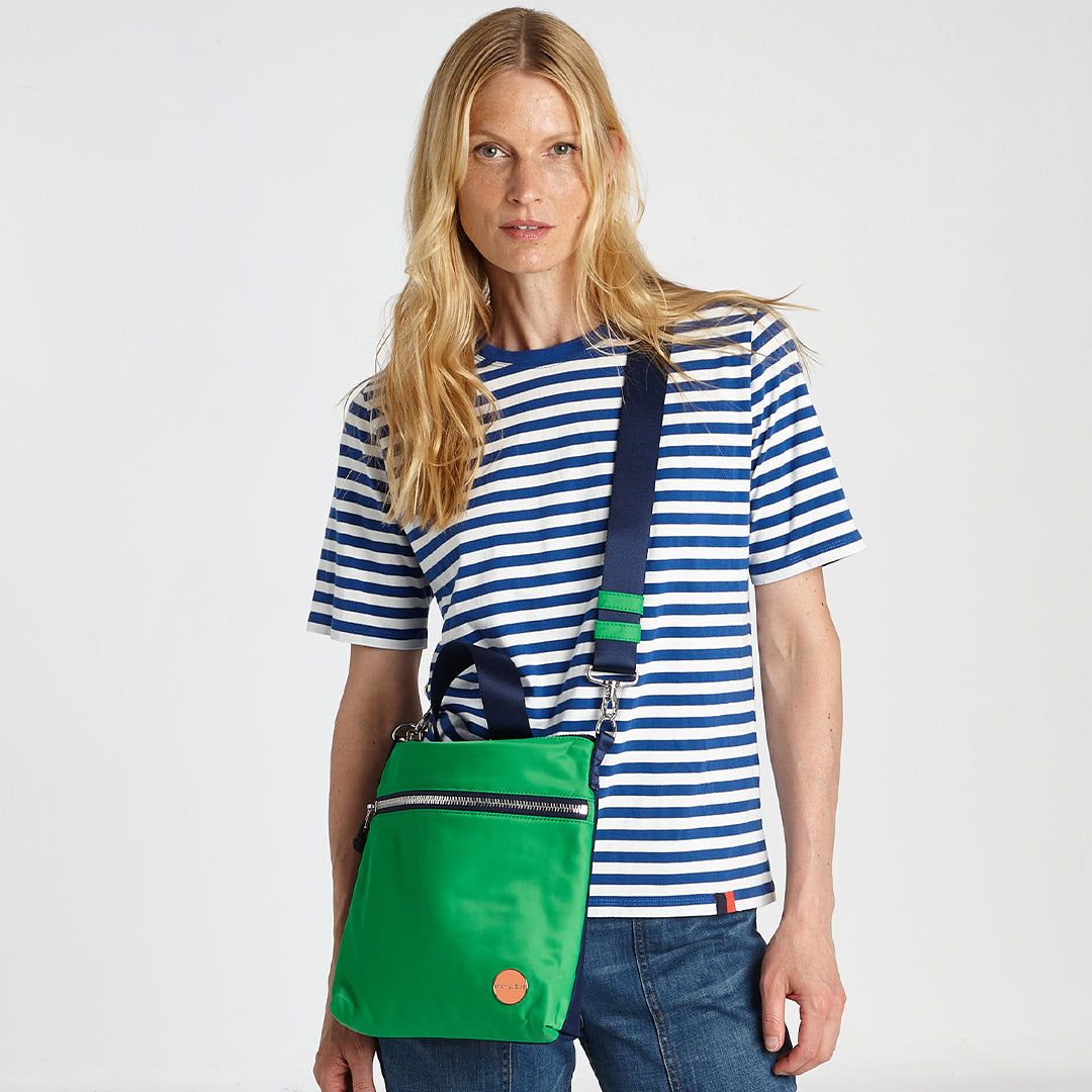 shortyLOVE amuse medium sized crossbody bag in grass green/navy; on model in striped top and jeans against white background.