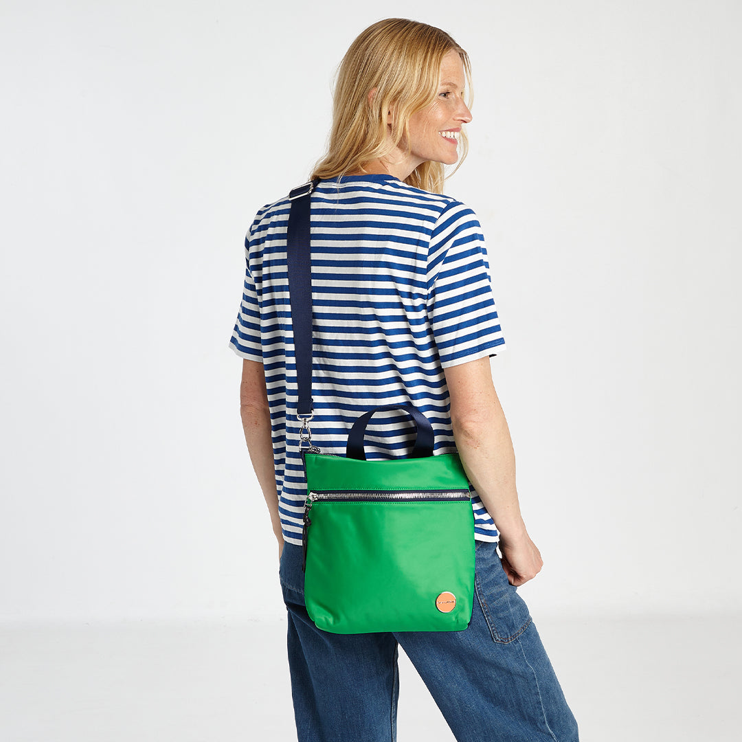 shortyLOVE amuse medium sized crossbody bag in grass green/navy; on model in striped top and jeans against white background.
