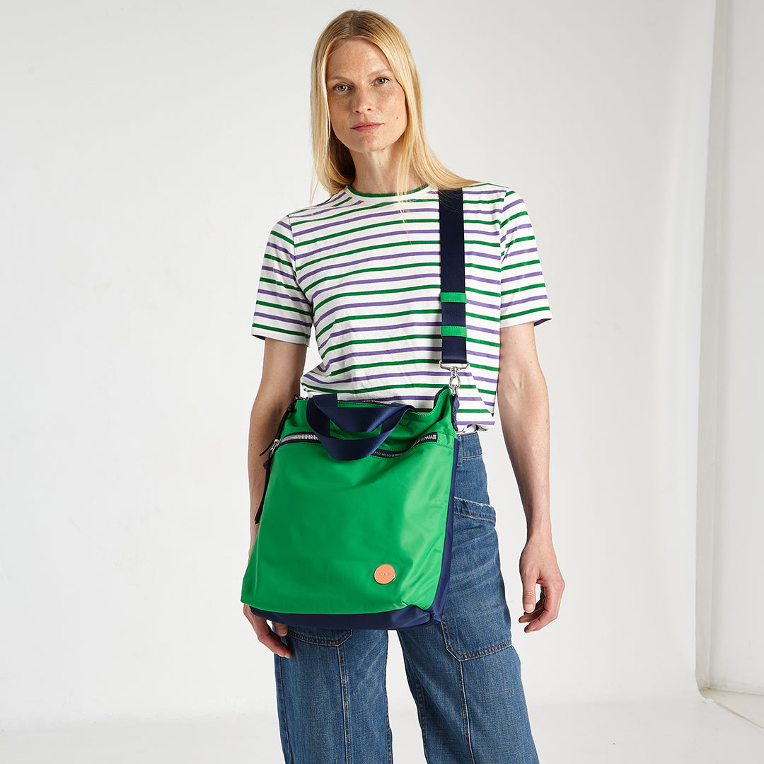 shortyLOVE wonder large crossbody/messenger bag in grass green/navy; on model in striped shirt and jeans against white background.