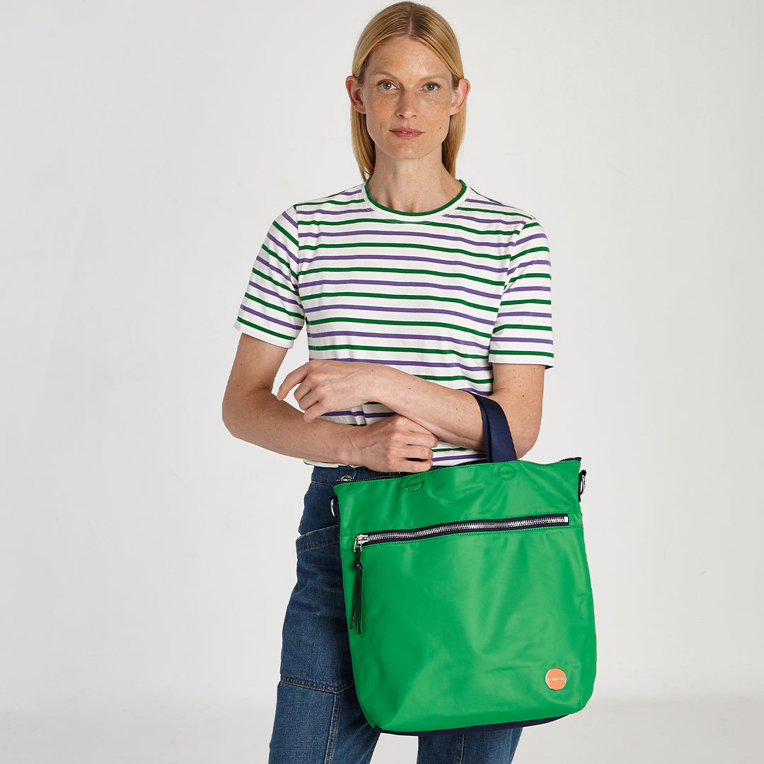 shortyLOVE wonder large crossbody/messenger bag in grass green/navy; on model in striped shirt and jeans against white background.