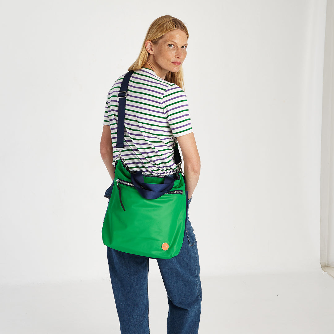 shortyLOVE wonder large crossbody/messenger bag in grass green/navy; on model in striped shirt and jeans against white background.