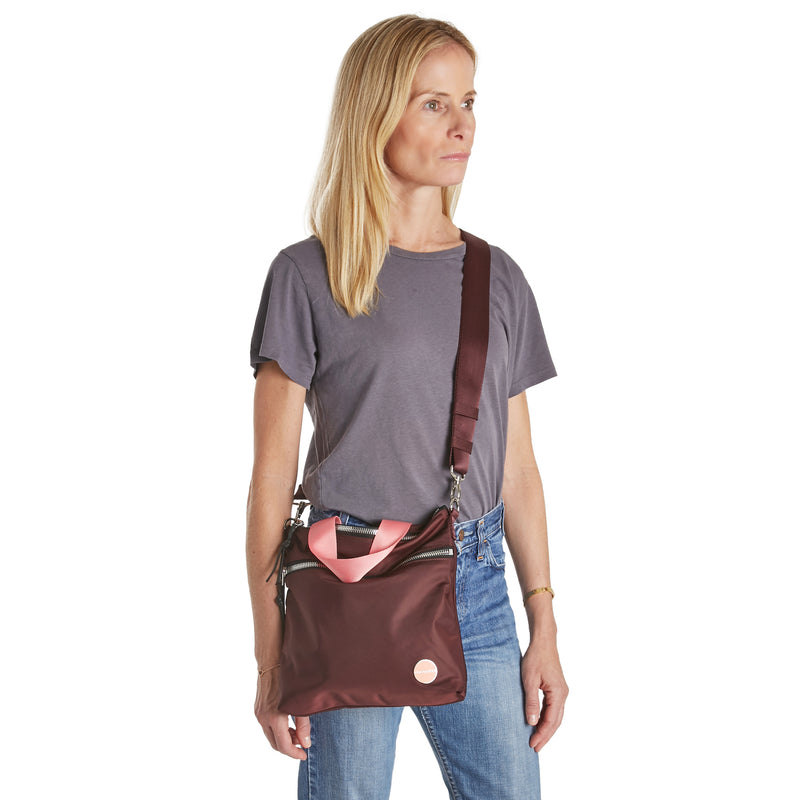 shortyLOVE amuse medium sized crossbody bag in burgundy; on model in grey top and jeans against white background.