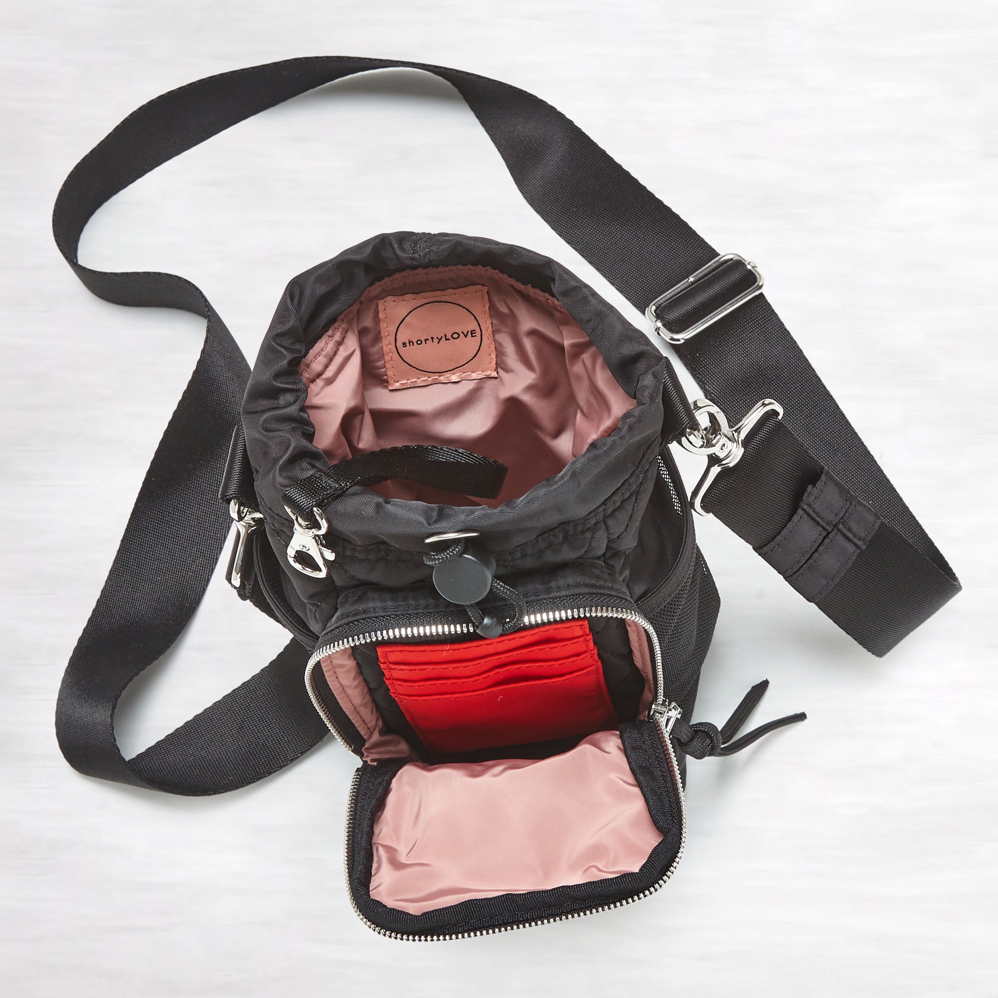 shortyLOVE bea sling bag in black; top-down view showing interior blush lining against grey background.