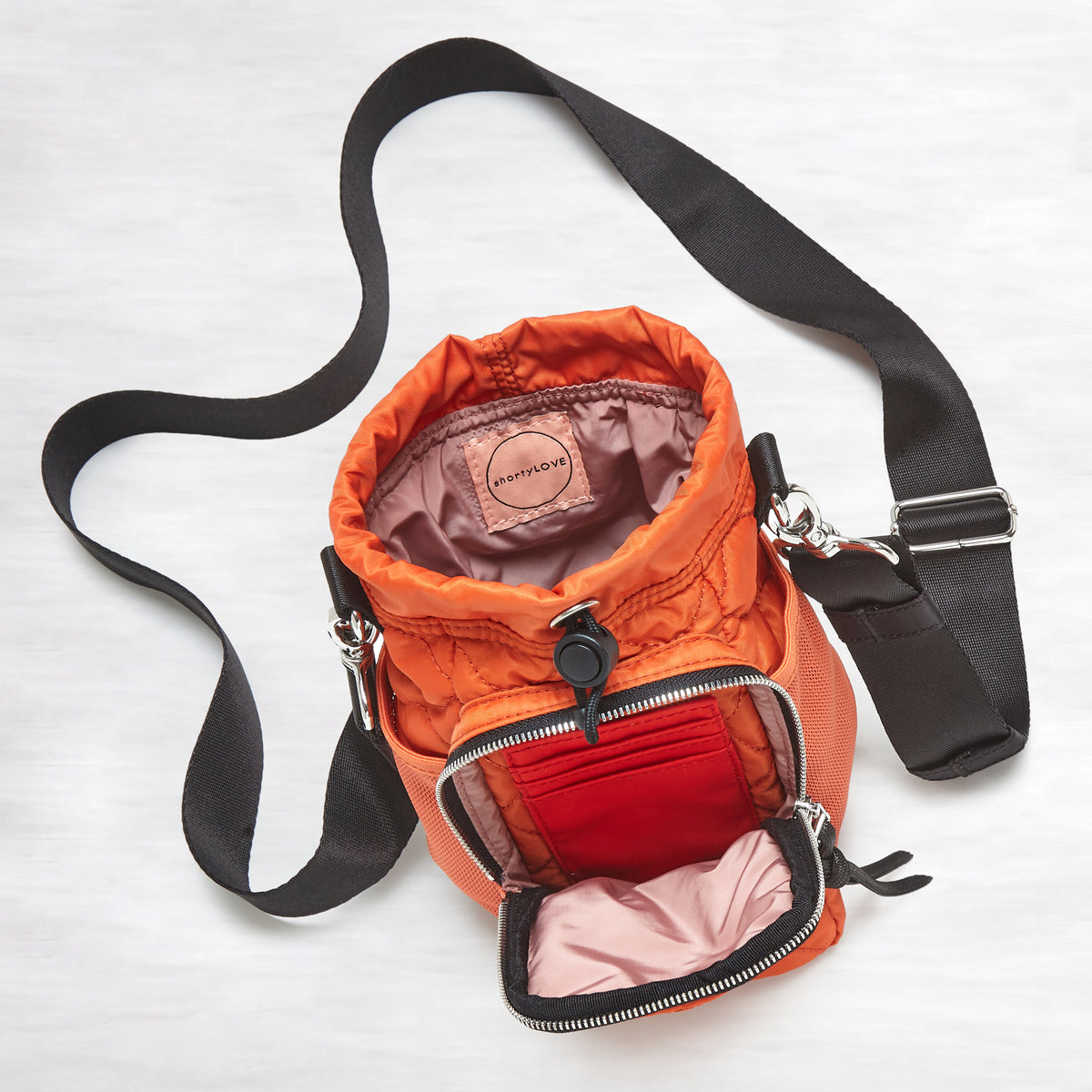 shortyLOVE bea sling bag in orange; top-down view showing interior blush lining against grey background.