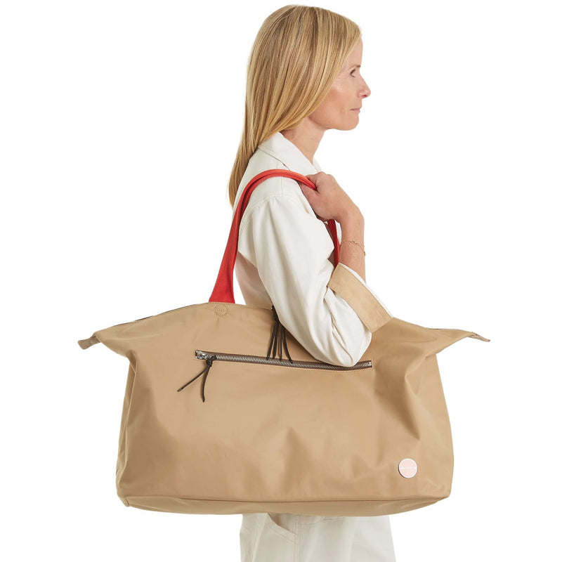 shortyLOVE friday weekender bag in khaki; on model’s shoulder in white jumpsuit against white background.