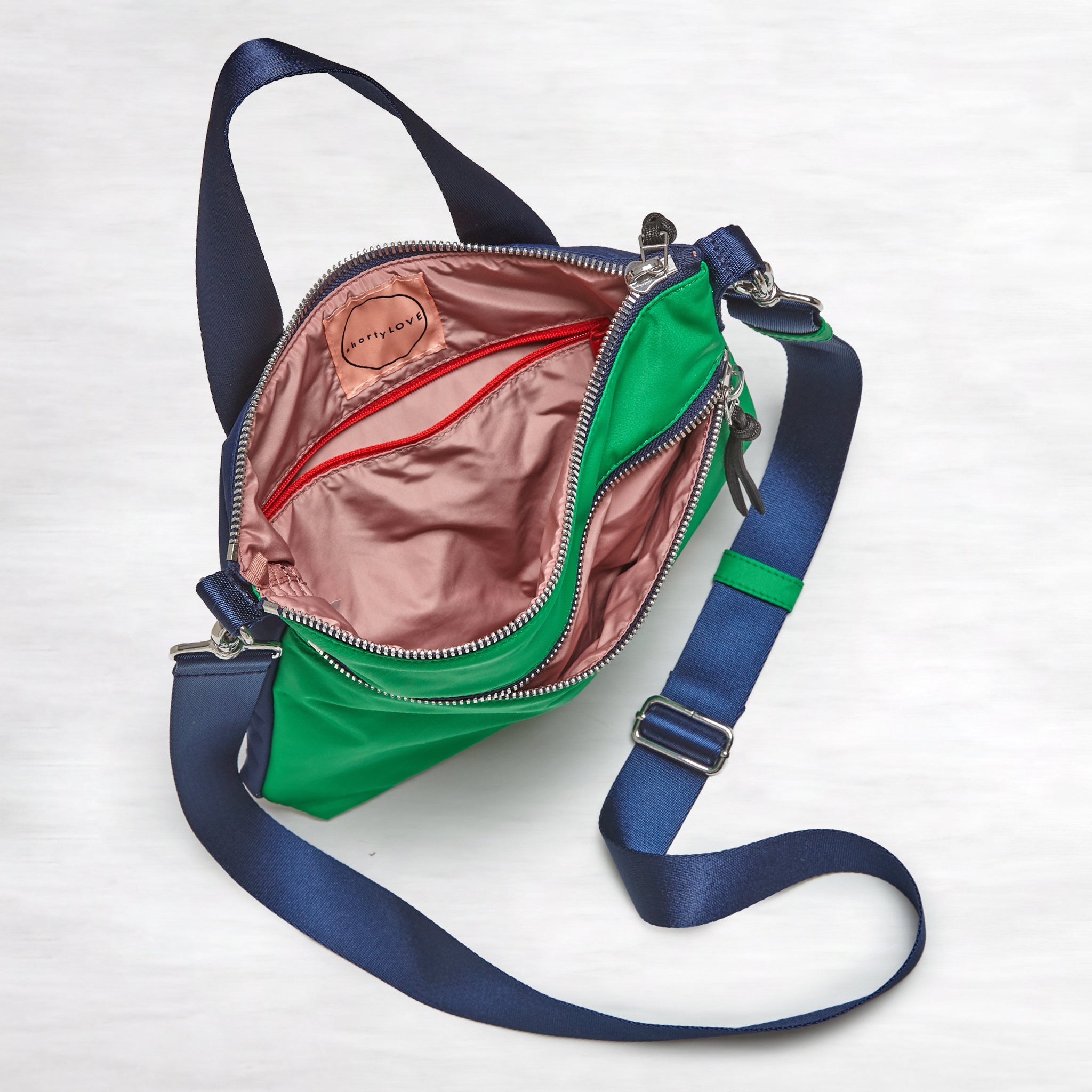 shortyLOVE amuse medium sized crossbody bag in grass green/navy; top-down view showing interior blush/red lining against white background.
