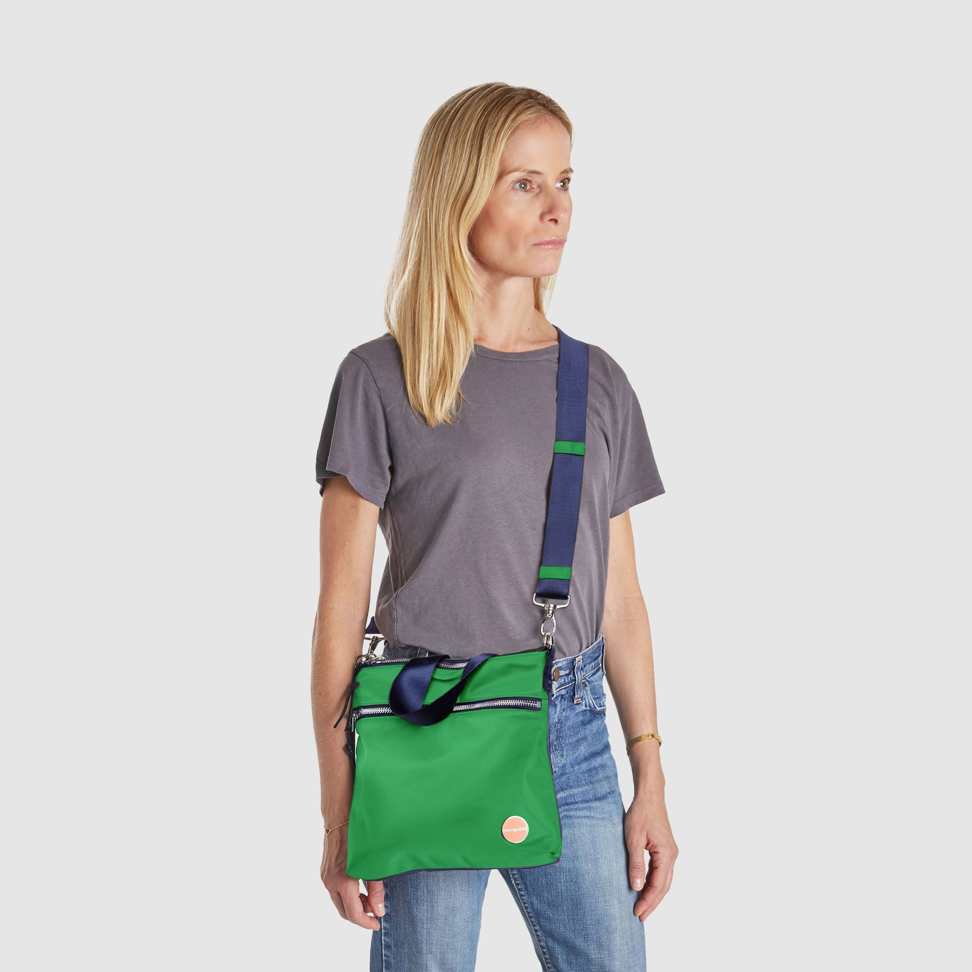 shortyLOVE amuse medium sized crossbody bag in grass green/navy; on model in grey top and jeans against white background.