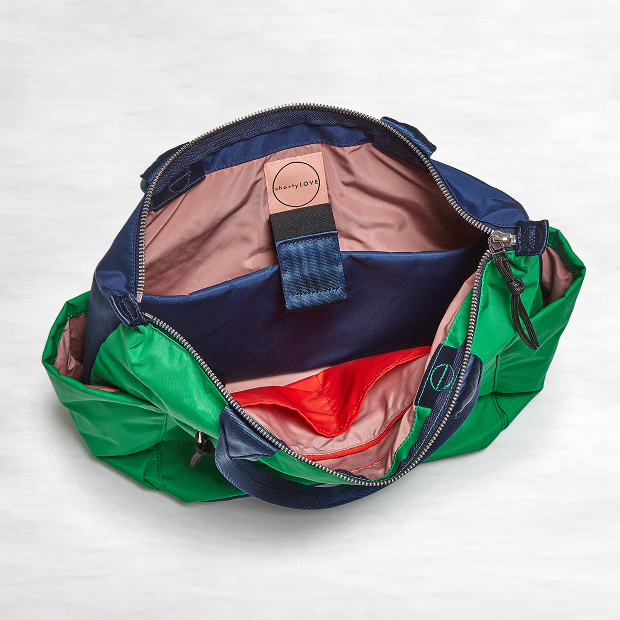 shortyLOVE wonder large crossbody/messenger bag in grass green/navy; top-down view showing interior blush/red lining against white background.