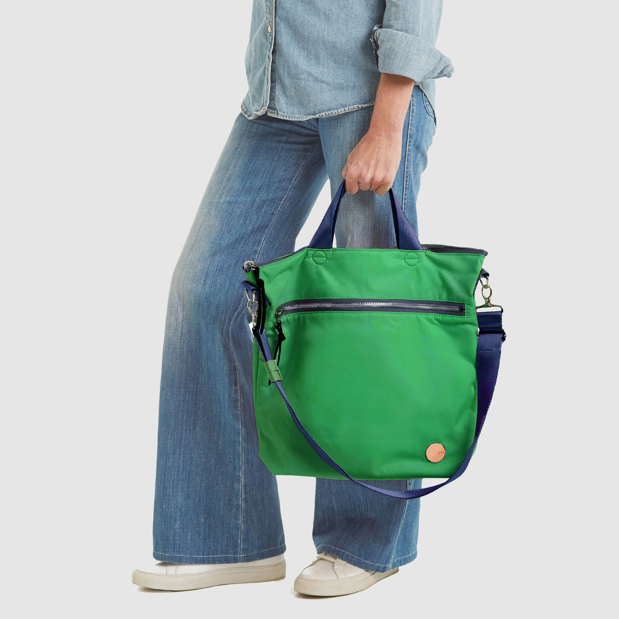 shortyLOVE wonder large crossbody/messenger bag in grass green/navy; hand held by model in jeans against white background.
