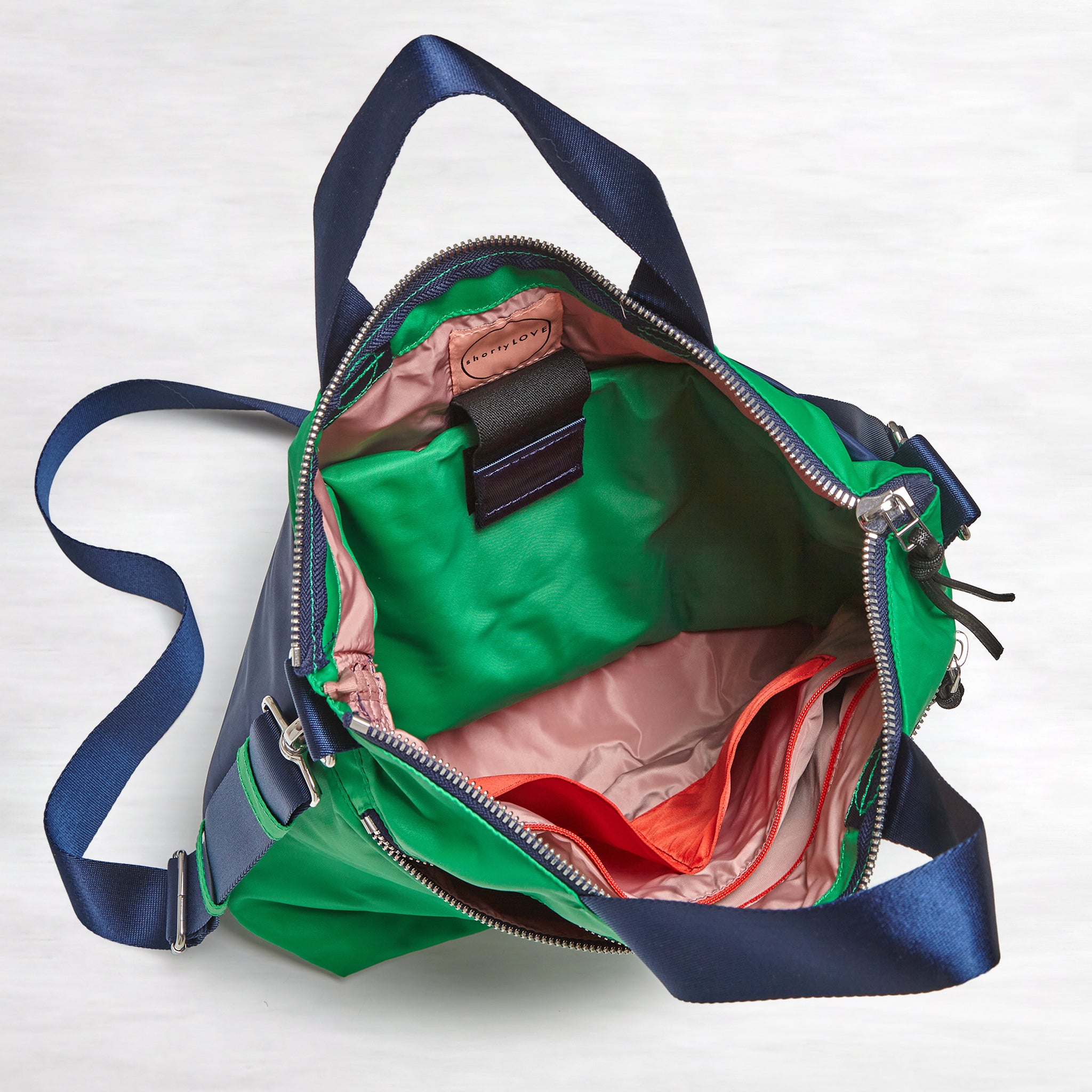 shortyLOVE wonder large crossbody/messenger bag in grass green/navy; top-down view showing interior blush/red lining against white background.