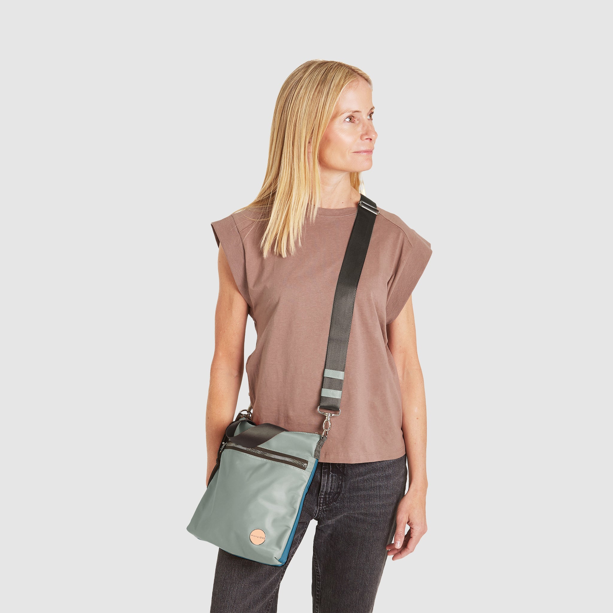 shortyLOVE amuse medium sized crossbody bag in slate/teal; on model in blush rose top and jeans against white background.