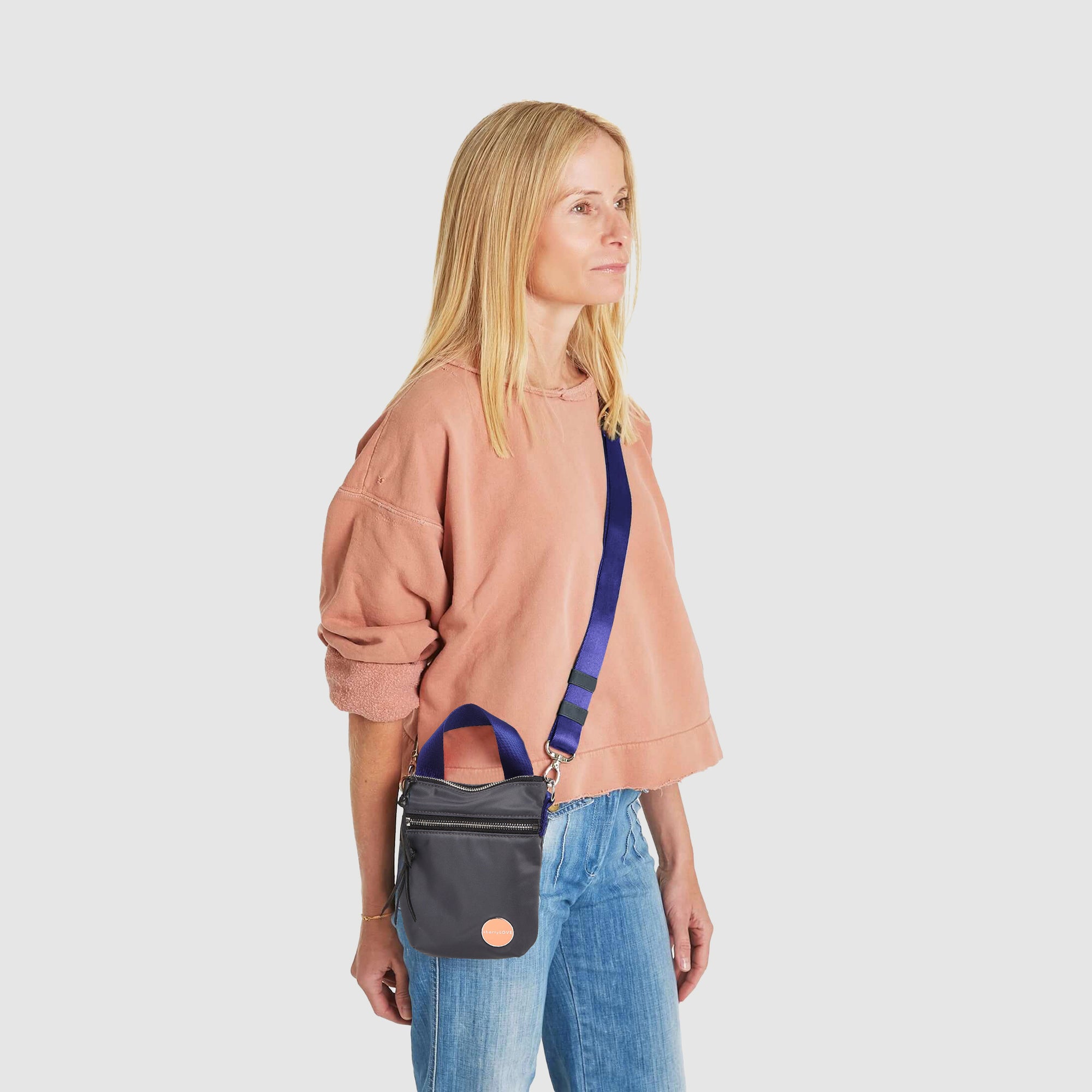 shortyLOVE shorthand small crossbody bag in charcoal; on model in peach sweatshirt and jeans against white background.