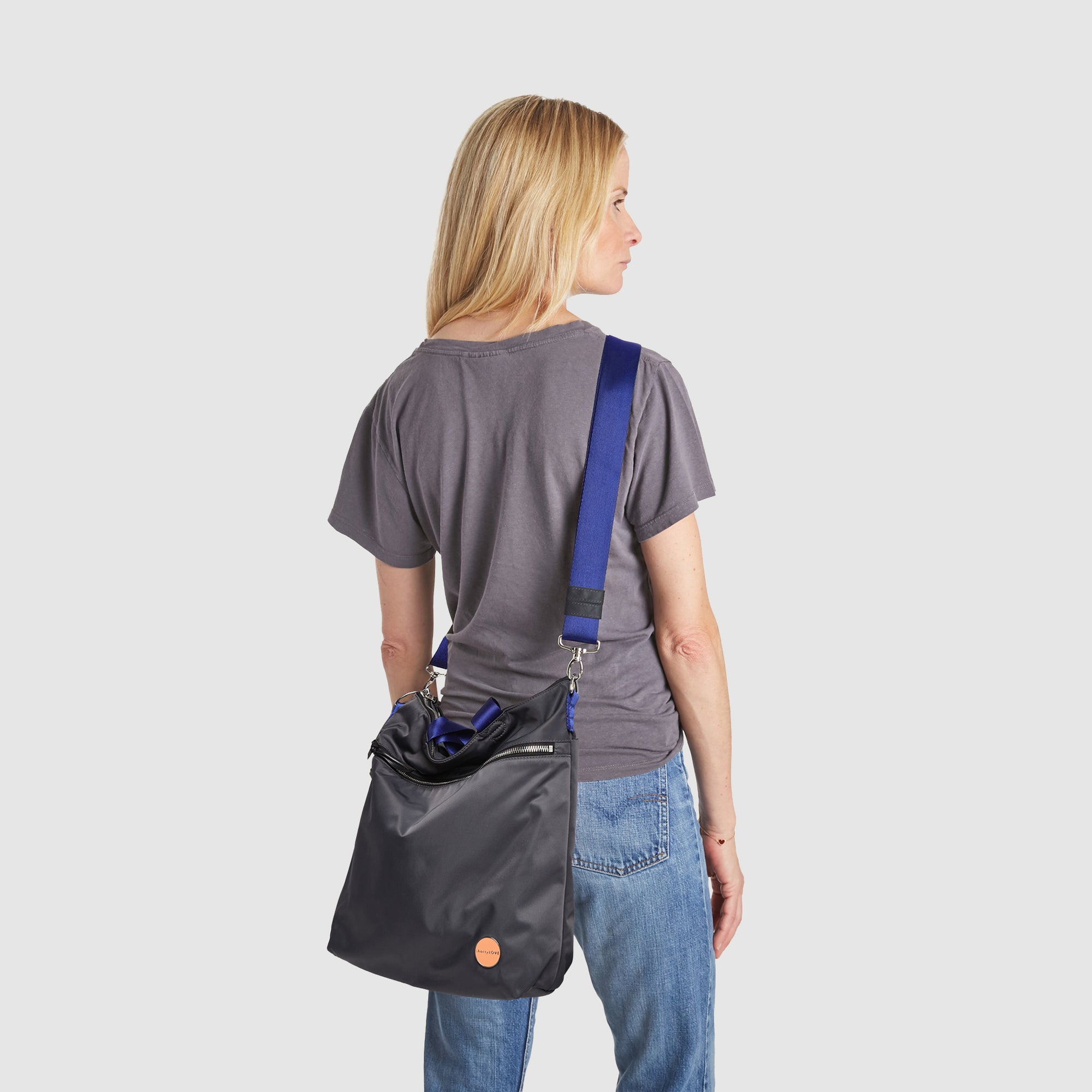 shortyLOVE wonder large crossbody/messenger bag in charcoal; on model in grey t-shirt and jeans against white background.