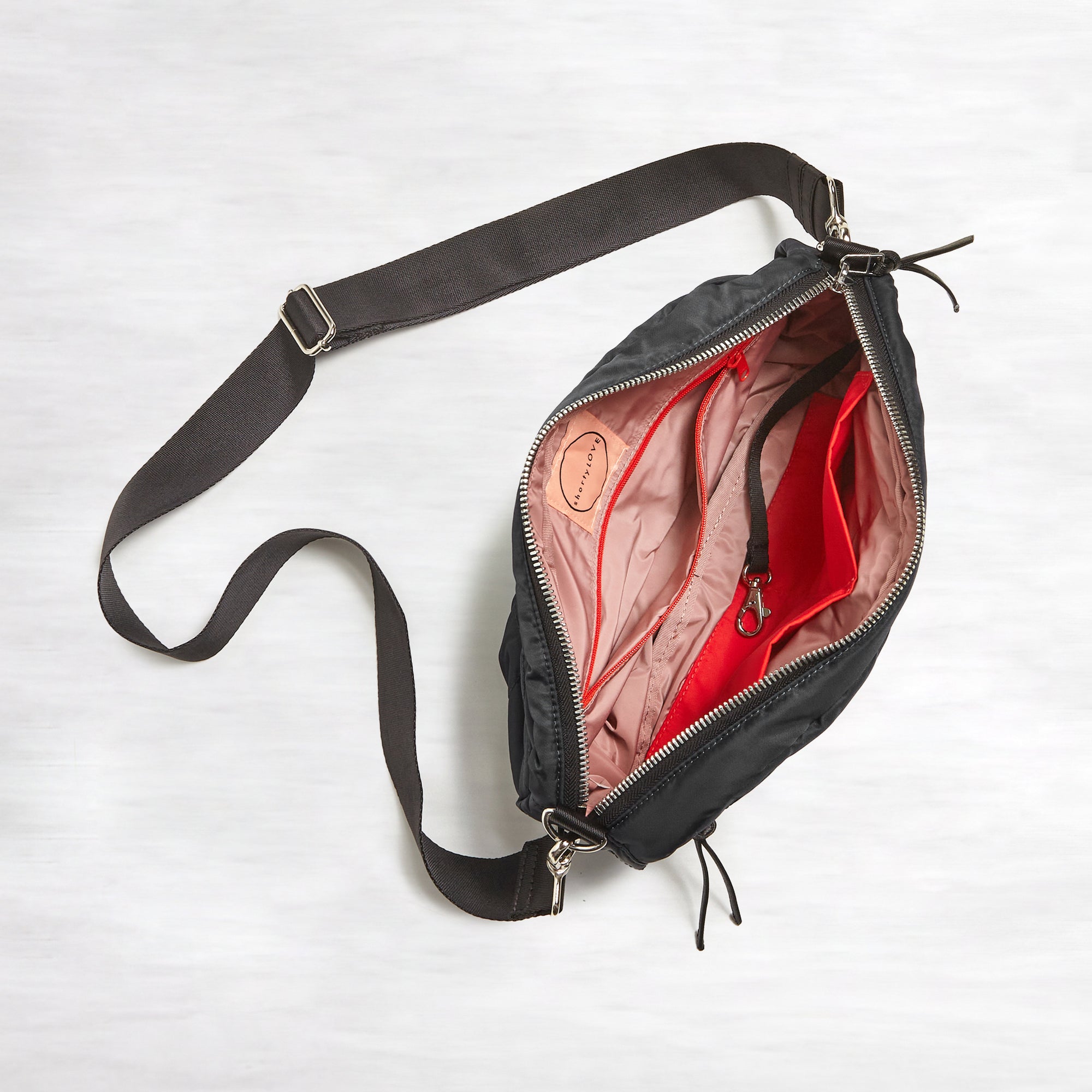 shortyLOVE cruiser medium crossbody bag in black; top-down view showing interior blush lining against white background.