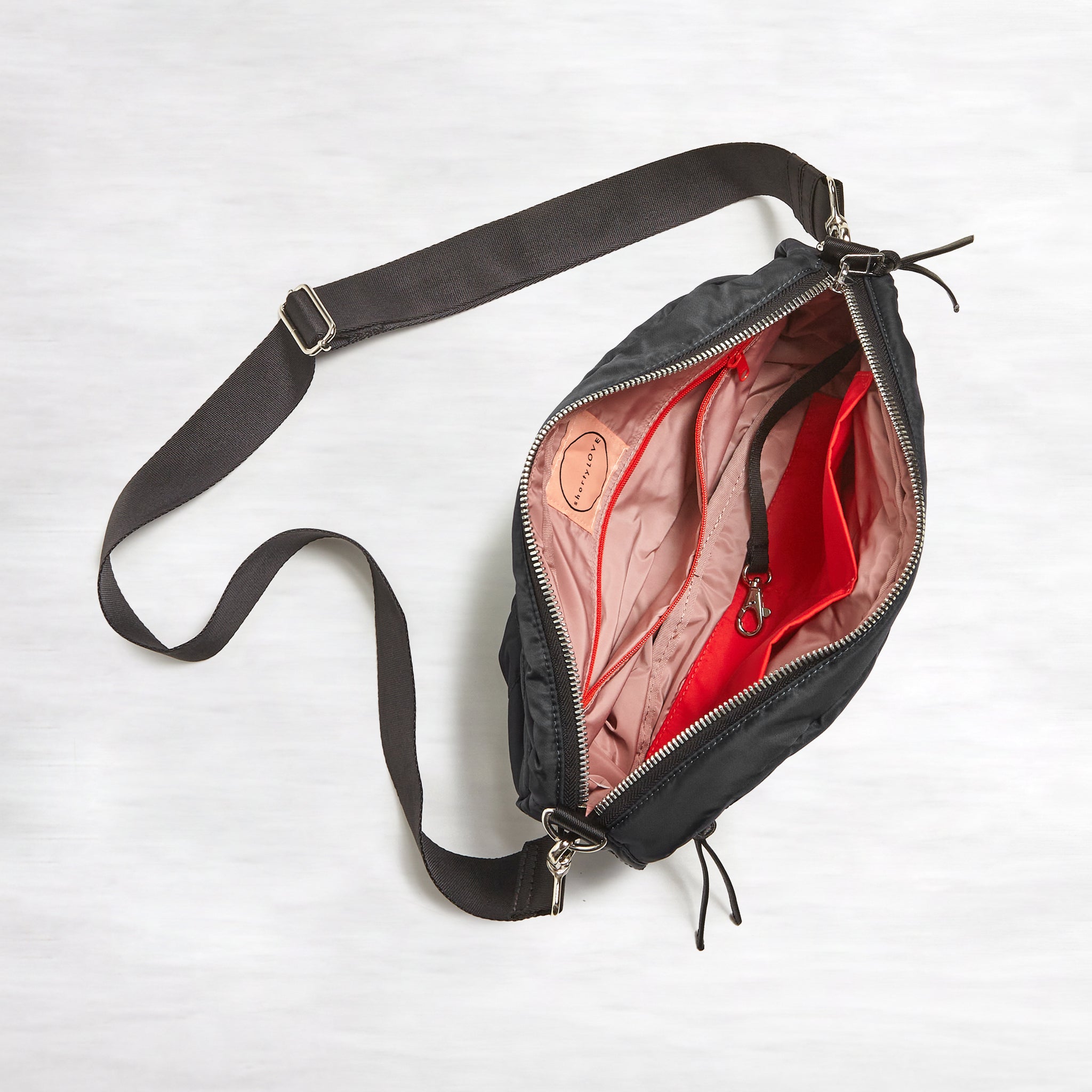 shortyLOVE cruiser medium crossbody bag in black; top-down view showing interior blush lining against white background.
