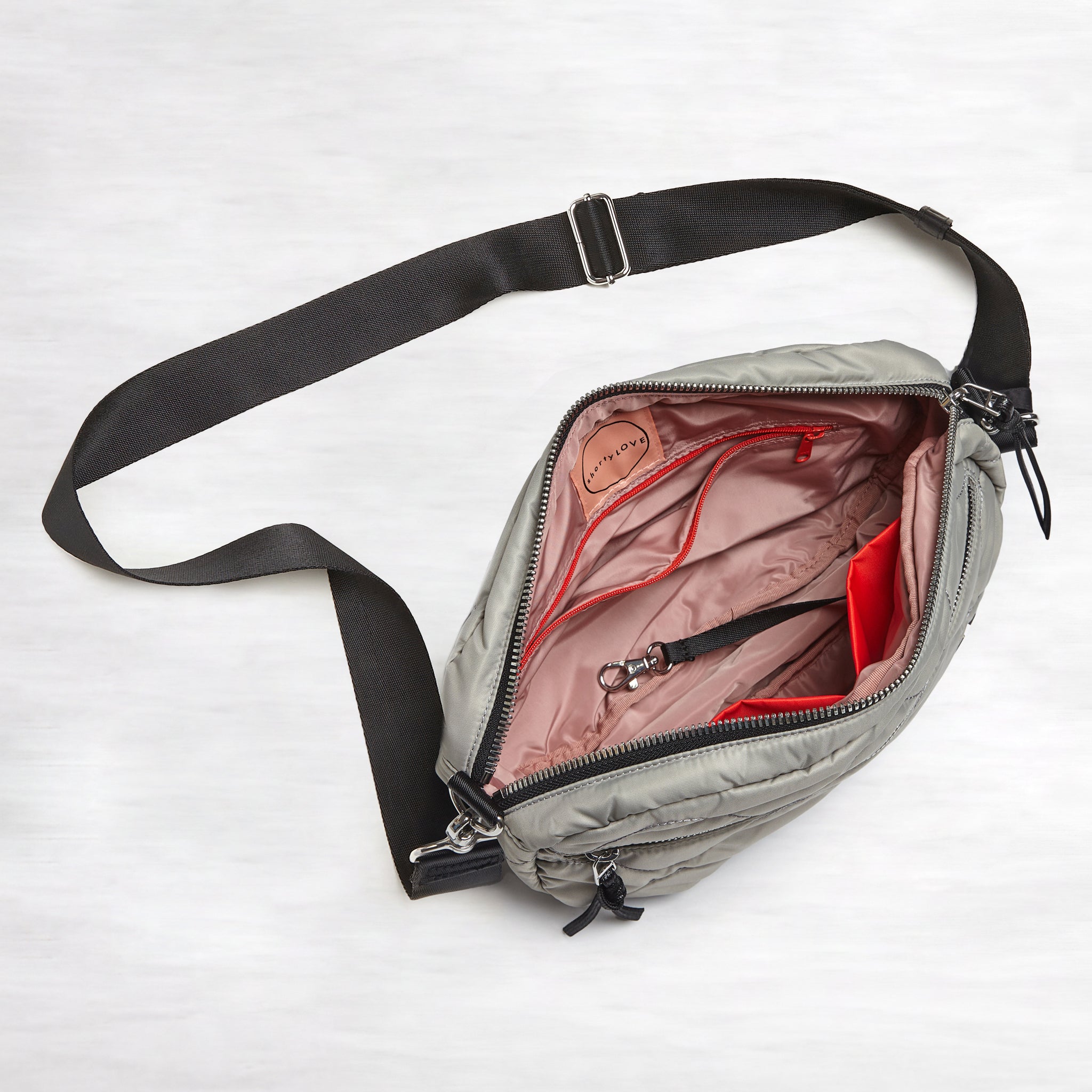 shortyLOVE cruiser medium crossbody bag in milky grey; top-down view showing interior blush lining against white background.