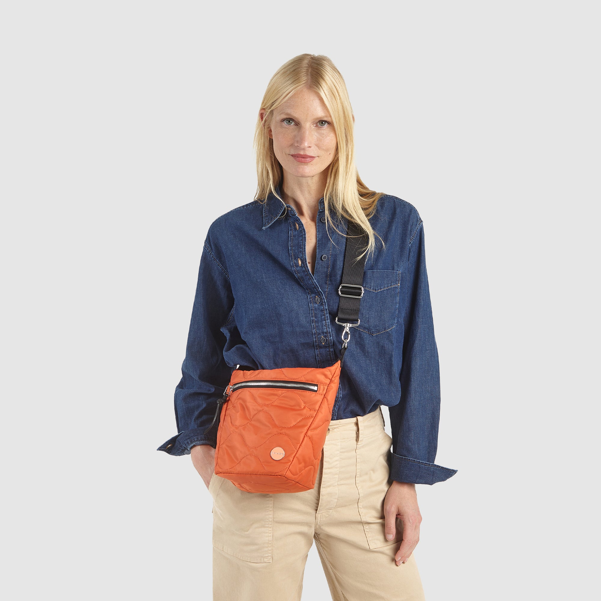 Woman wearing an orange marcel quilted crossbody bag on a white background
