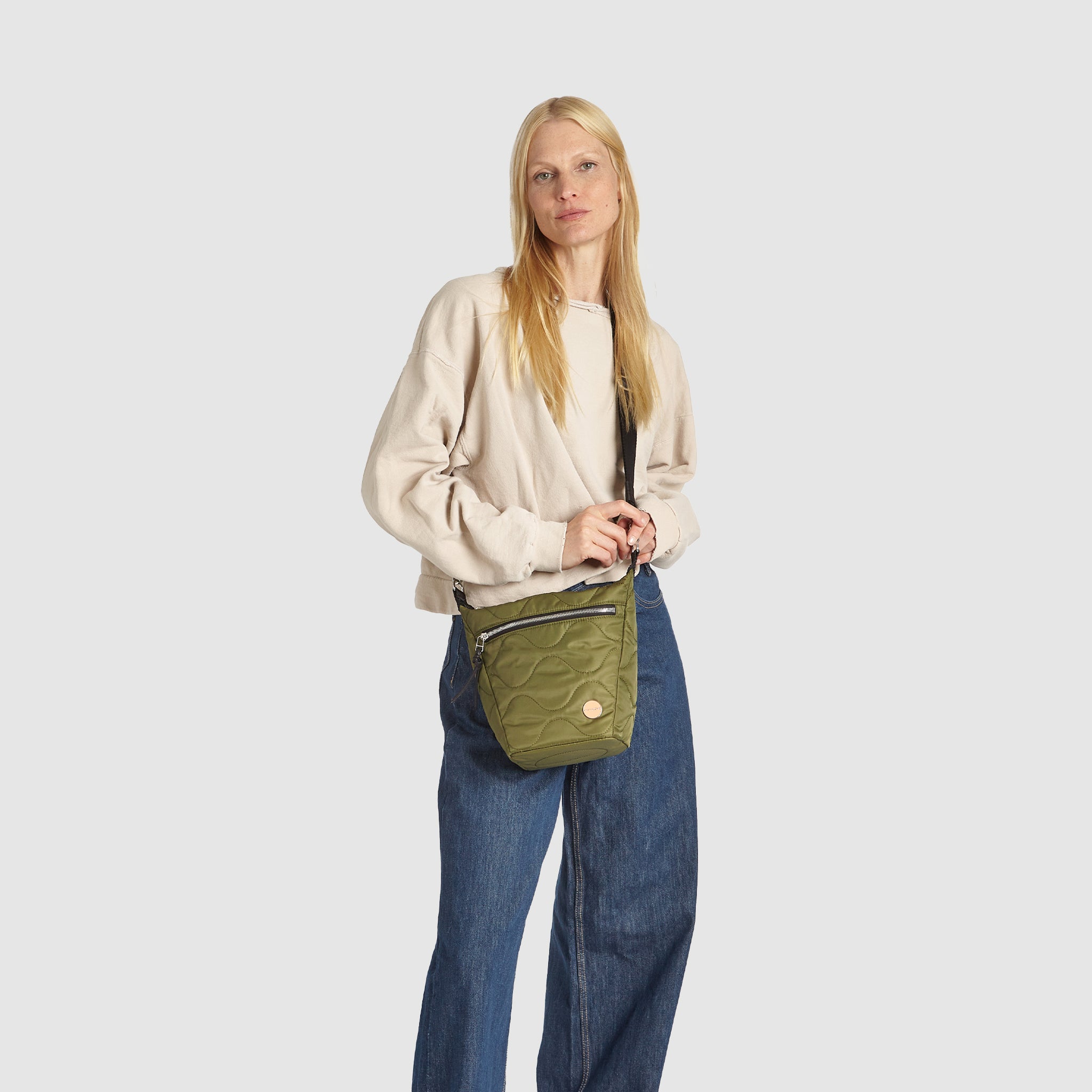 Woman wearing a sage green marcel quilted crossbody bag with a colorful crossbody strap on a white background