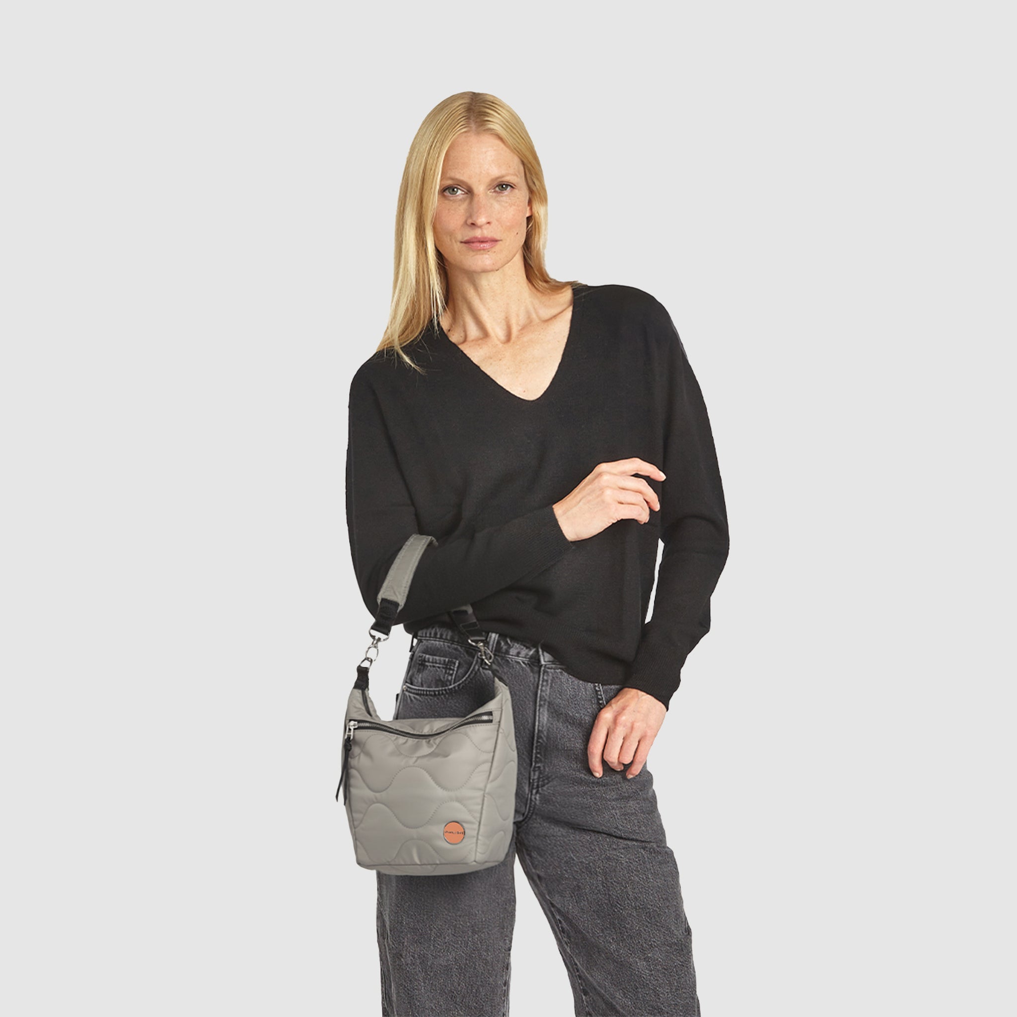 Woman holding a gray marcel quilted crossbody  handbag against a white background