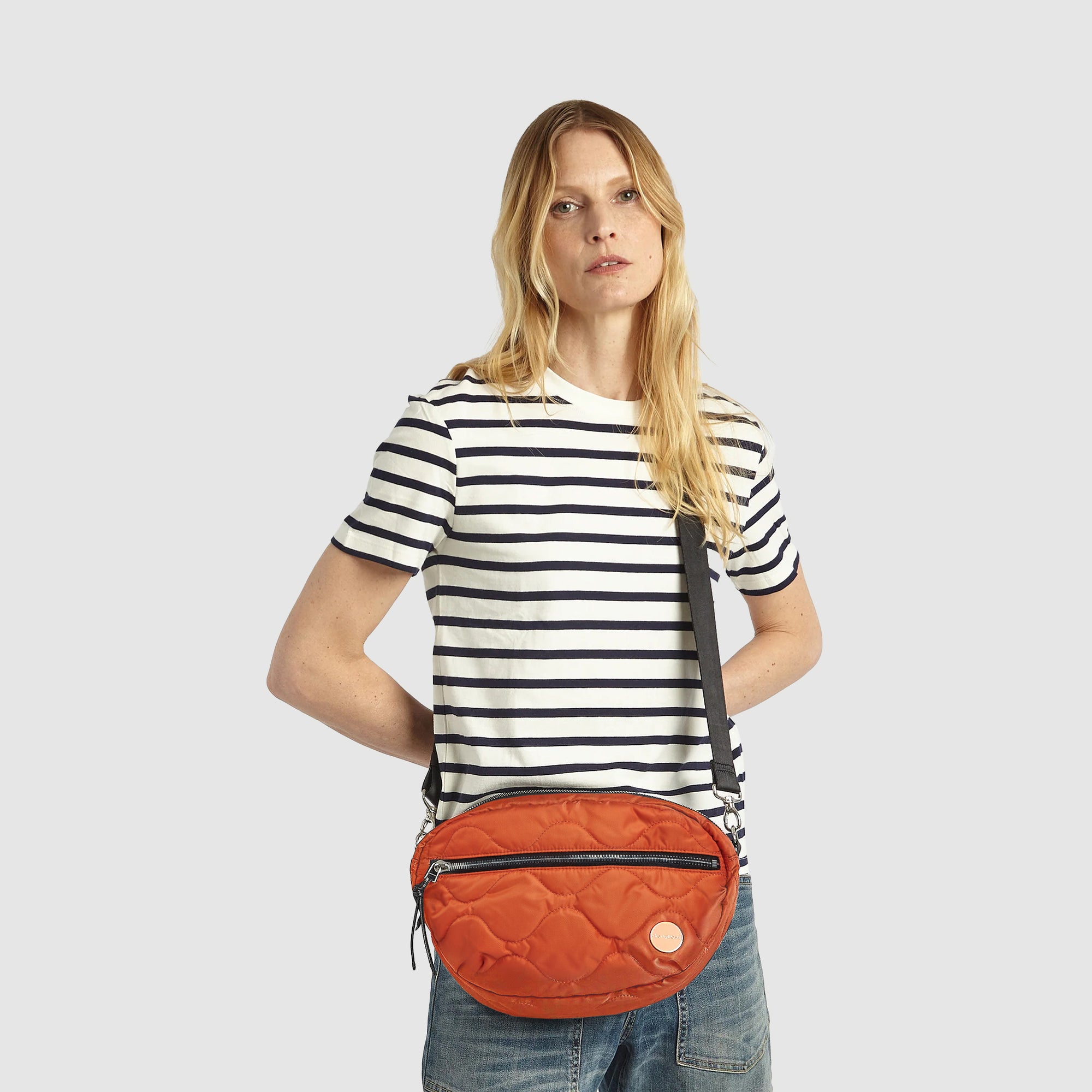 shortyLOVE cruiser medium crossbody bag in orange; on model in striped shirt and jeans against white background.
