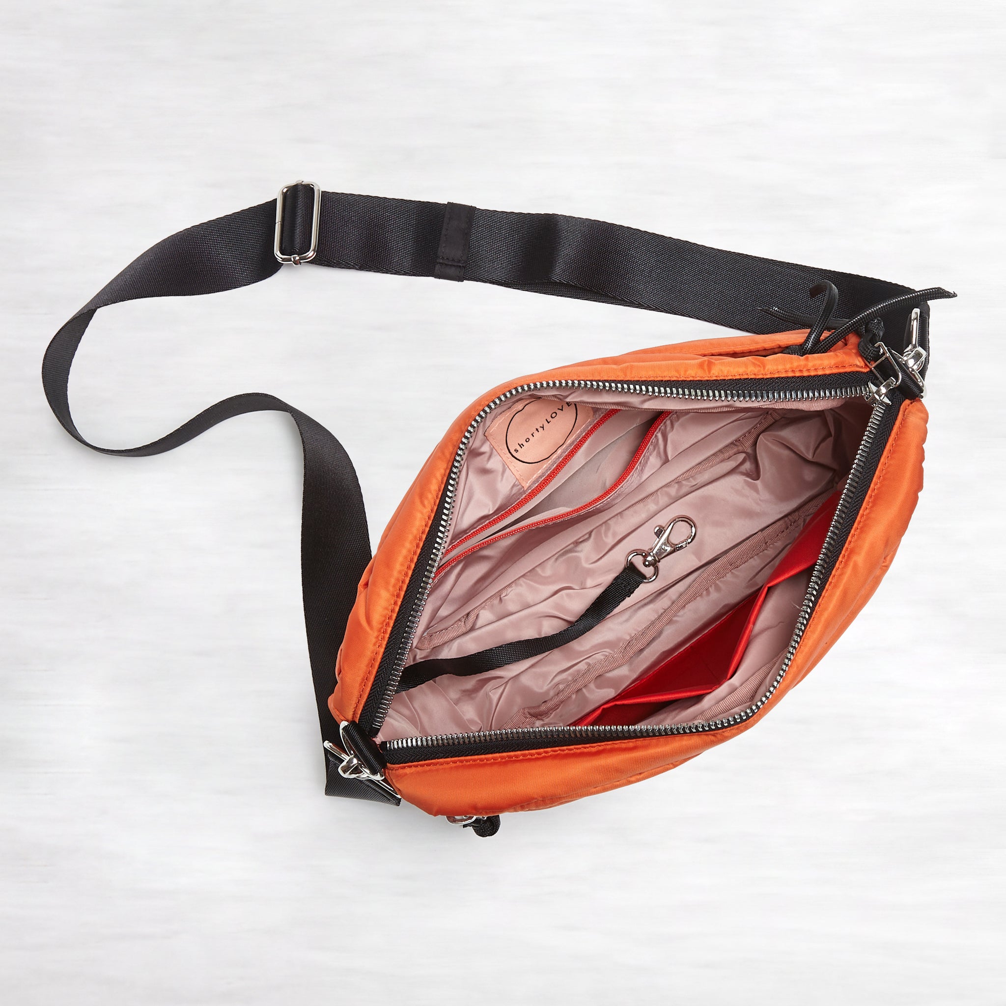 shortyLOVE cruiser medium crossbody bag in orange; top-down view showing interior blush lining against white background.