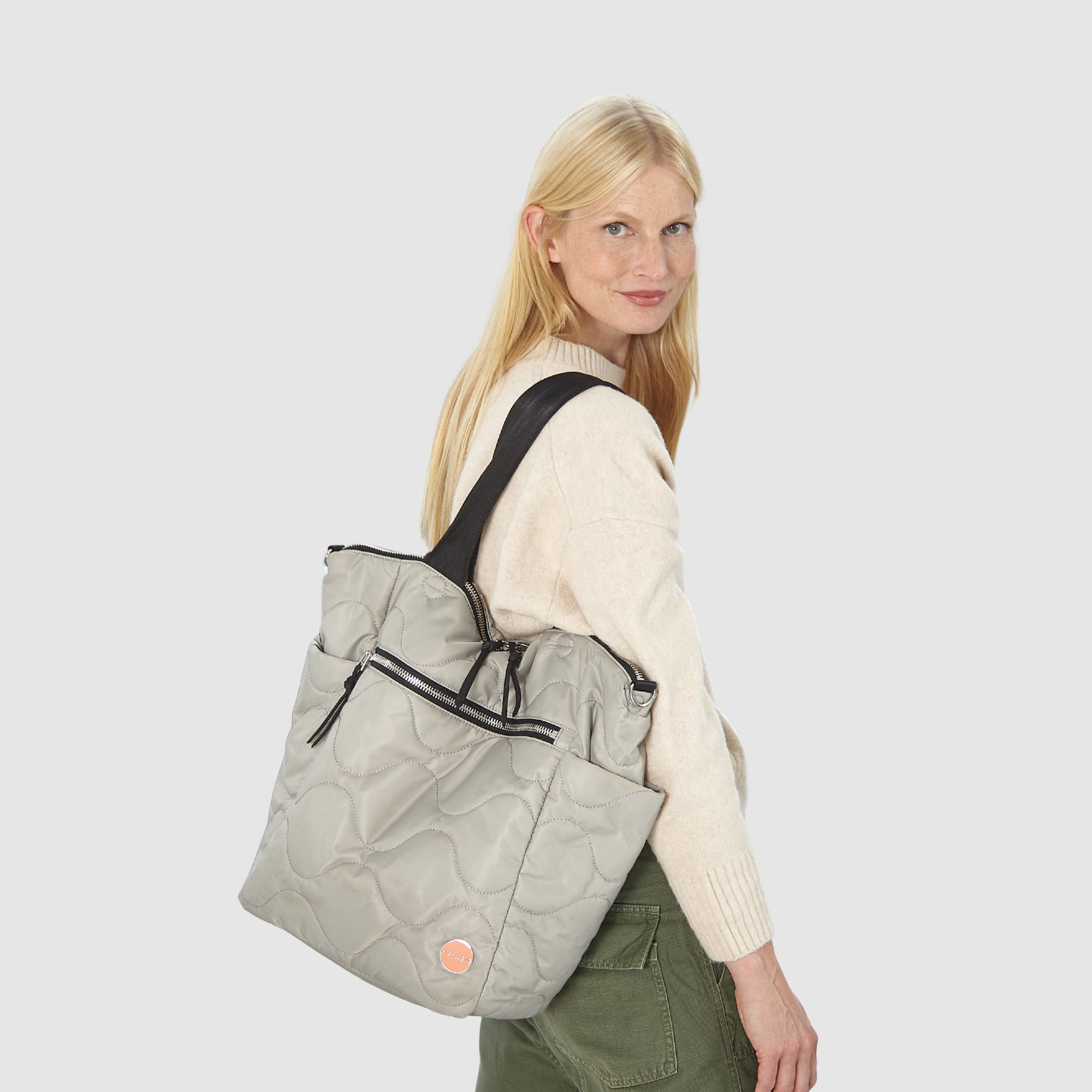 Woman sitting on a blue couch with a gray quilted ranger tote bag, surrounded by green plants.